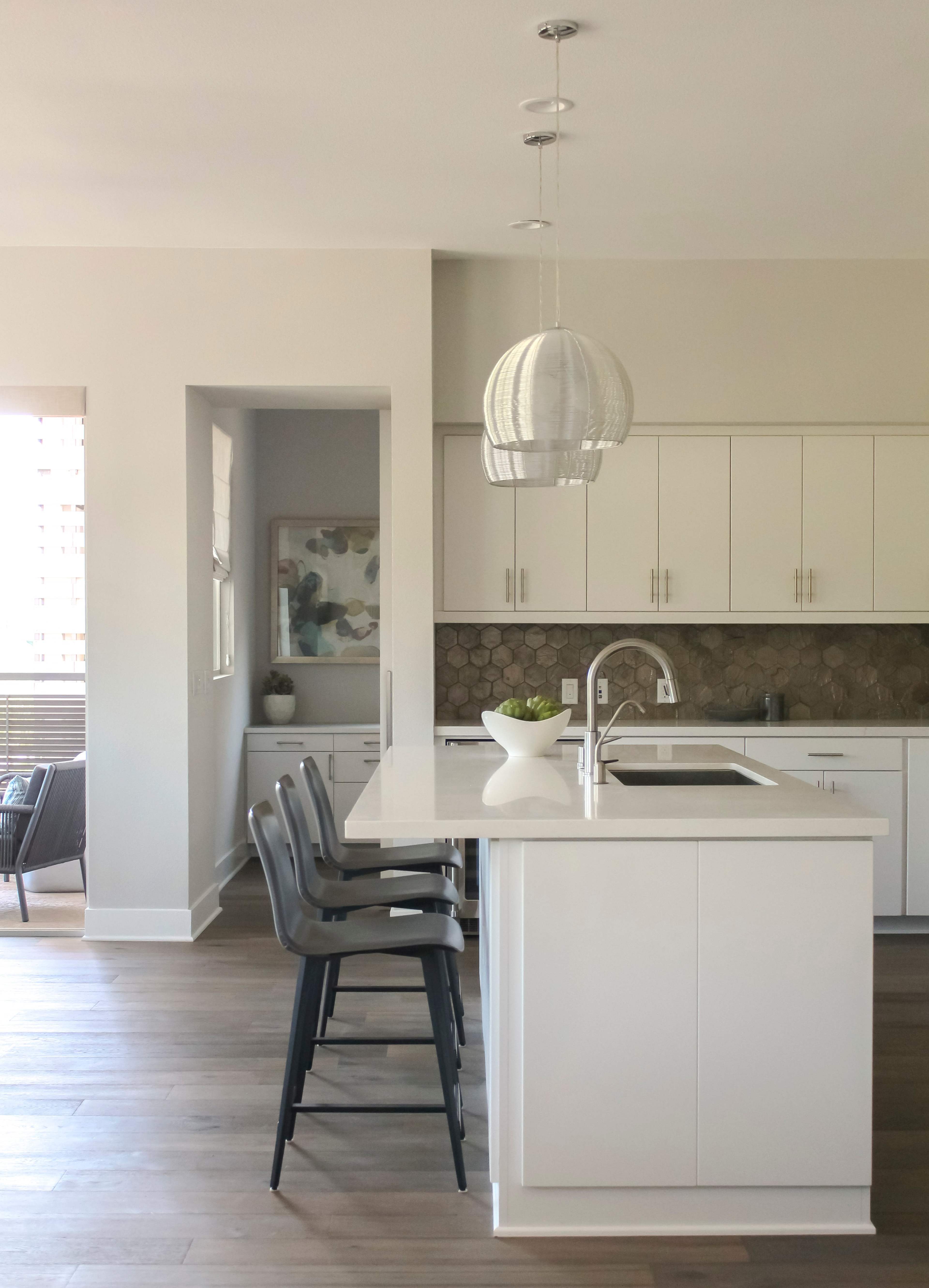 A modern kitchen features a central island with black stools, white cabinetry, and a pendant light hanging above.