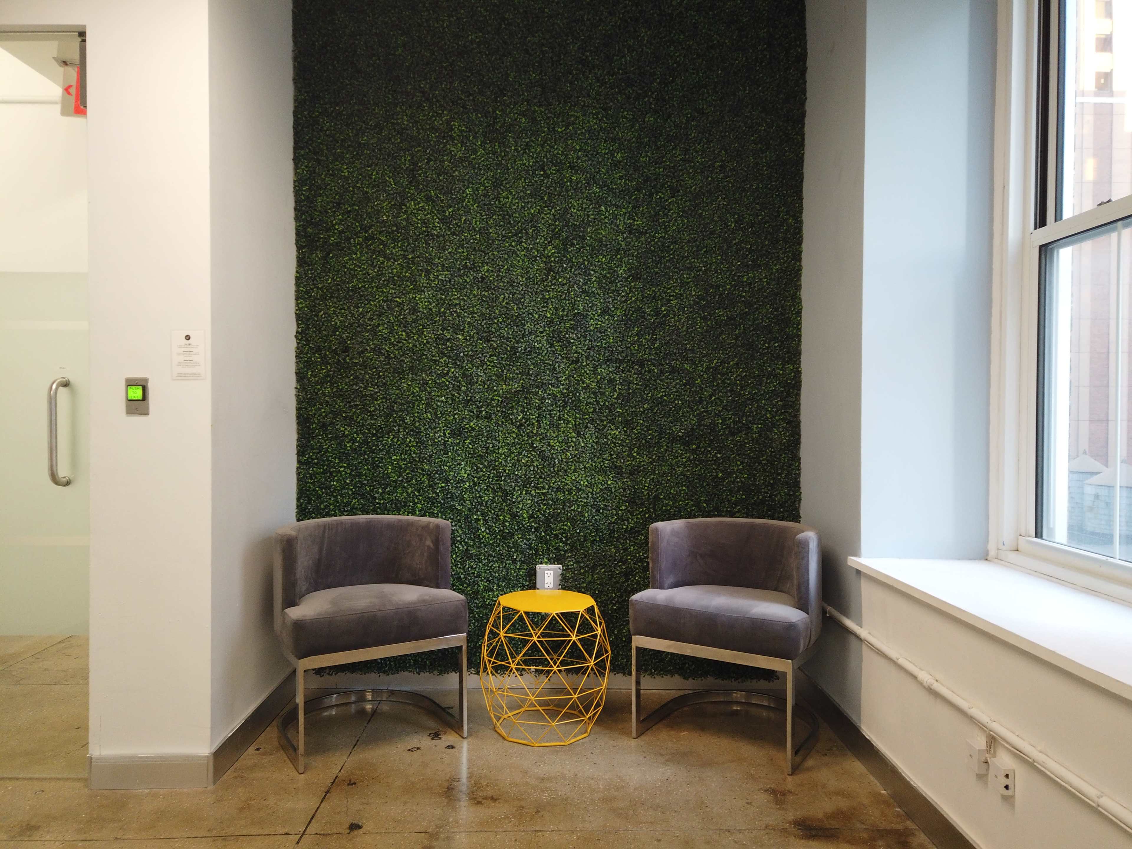 Two modern gray chairs are positioned facing each other next to a yellow geometric side table against a green wall.