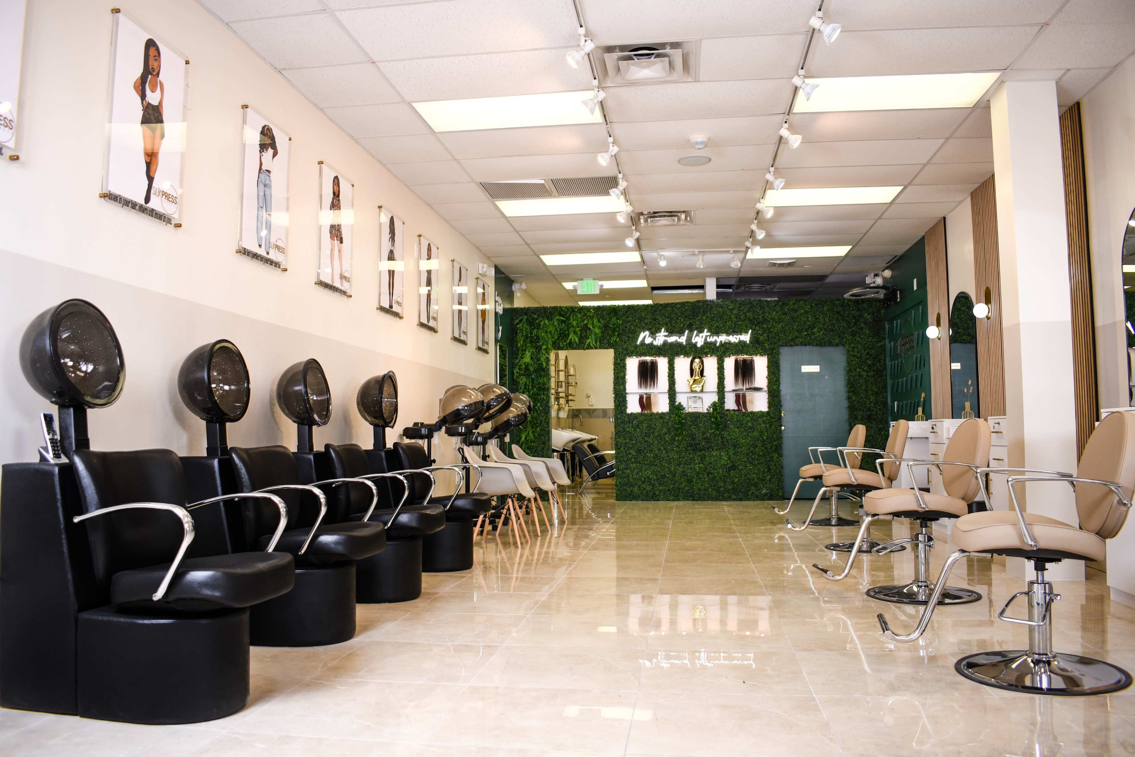 A modern hair salon features rows of black and beige styling chairs along a tiled floor, with framed photos on the walls and a green accent wall at the back.