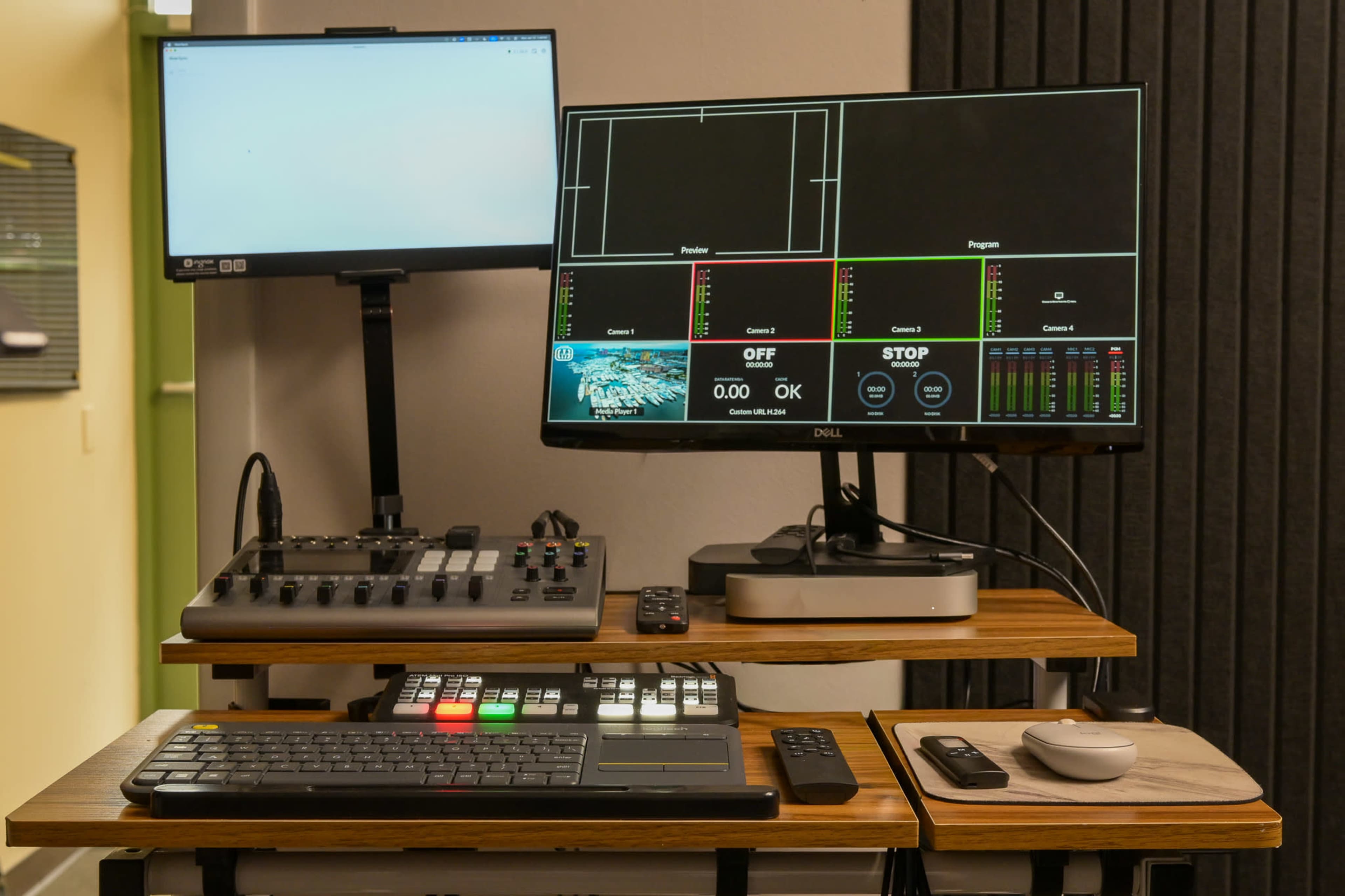 The image shows a broadcasting control station with two monitors, a video switcher, and various control devices on a wooden table.