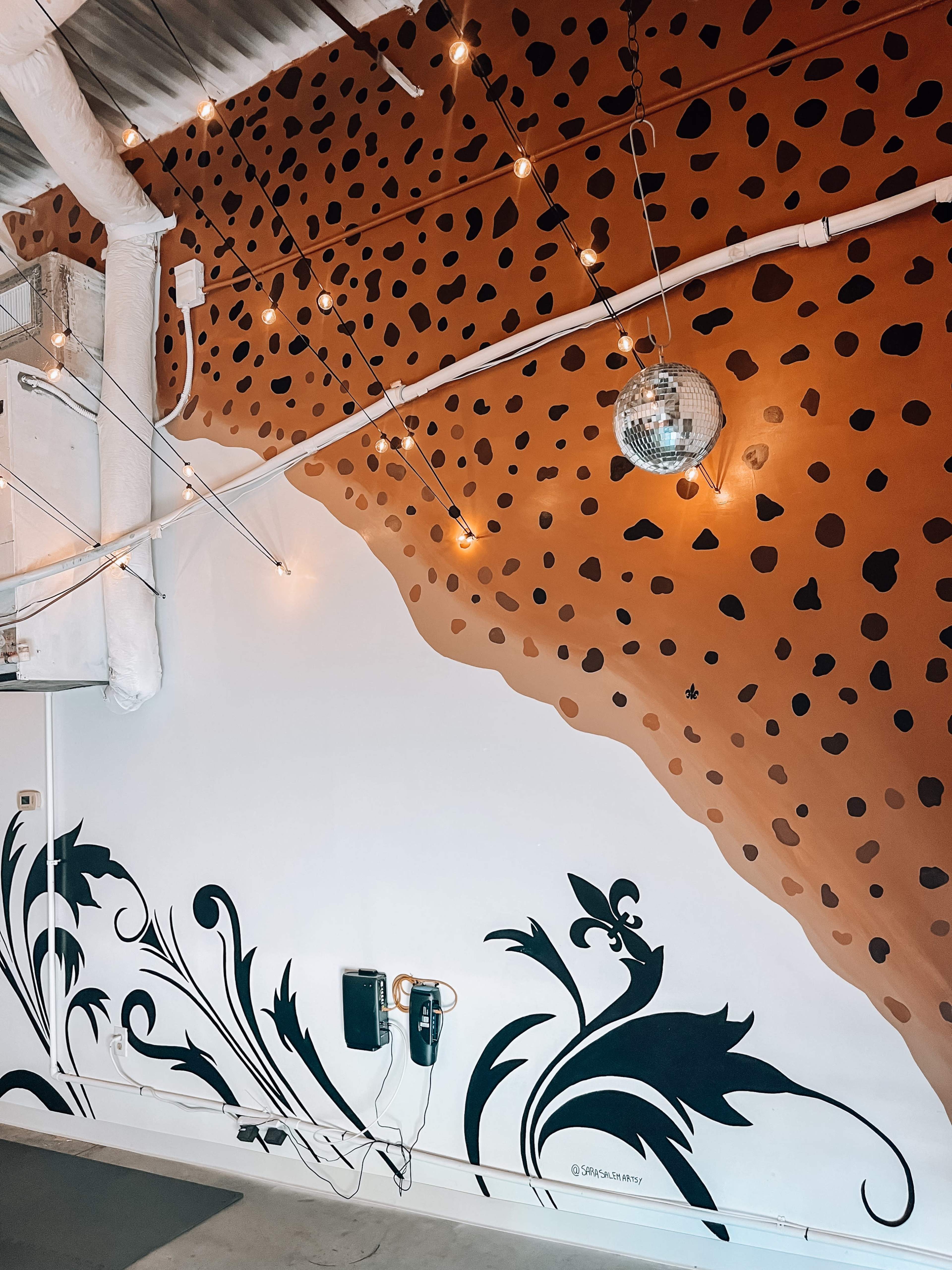 The image shows a wall featuring a brown spotted pattern at the top, with a black floral design at the bottom, and decorative string lights overhead.
