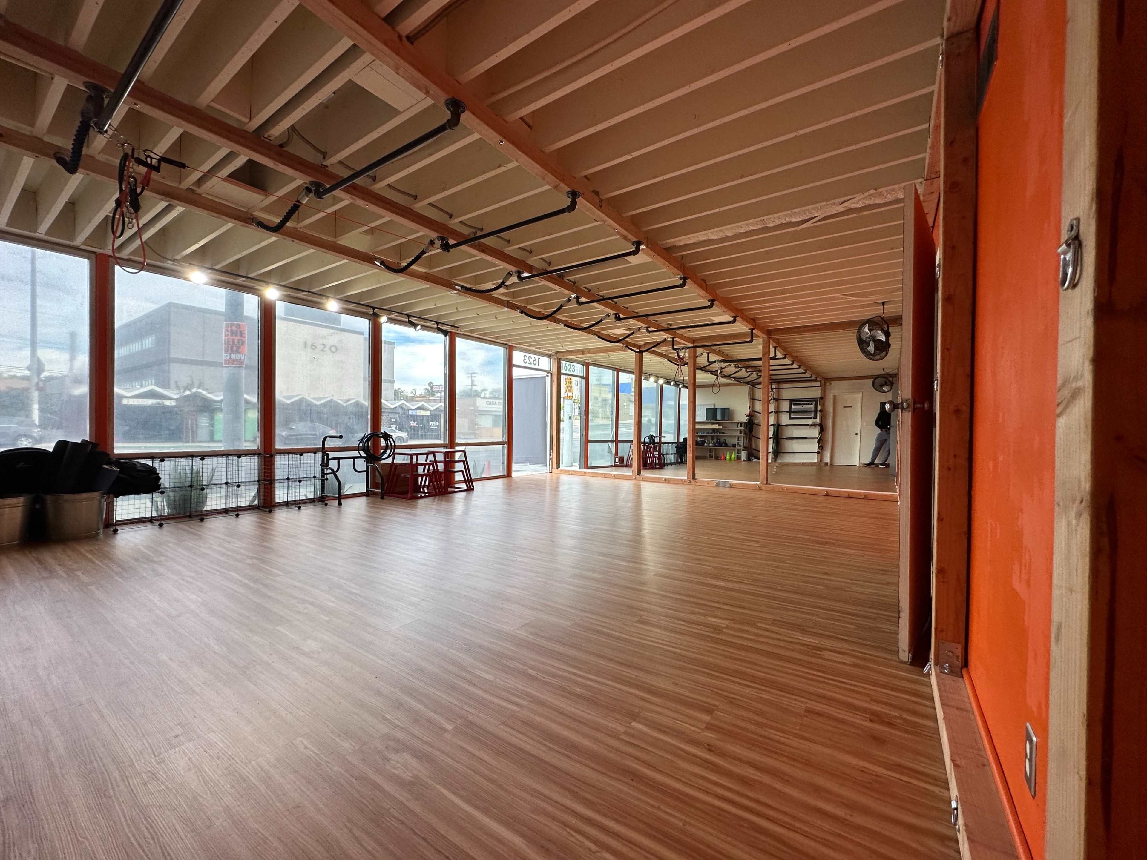 A spacious interior room with wooden flooring and large windows overlooking a cityscape.