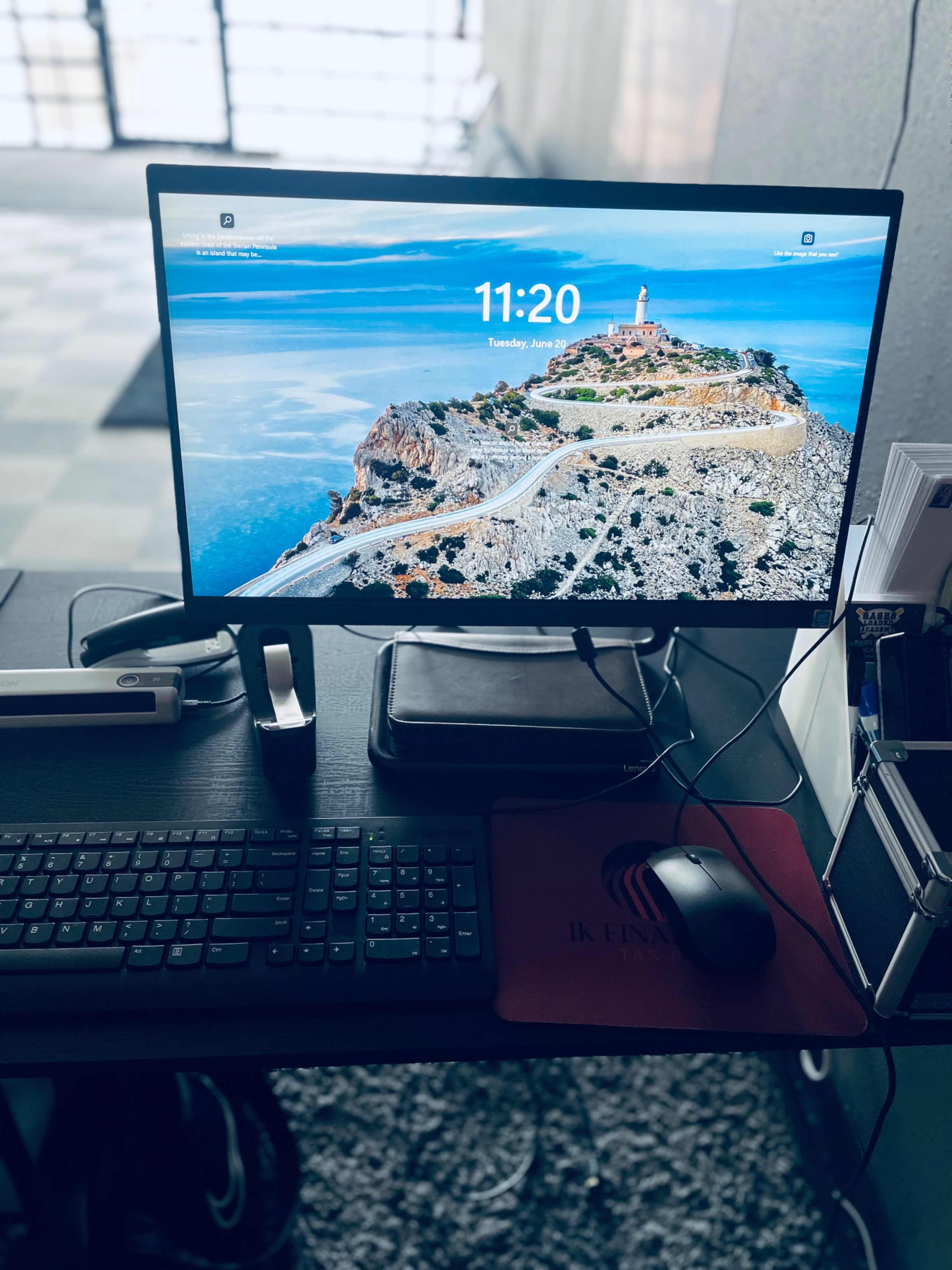 A computer monitor displaying a scenic landscape with a lighthouse, placed on a desk alongside a keyboard and mouse.