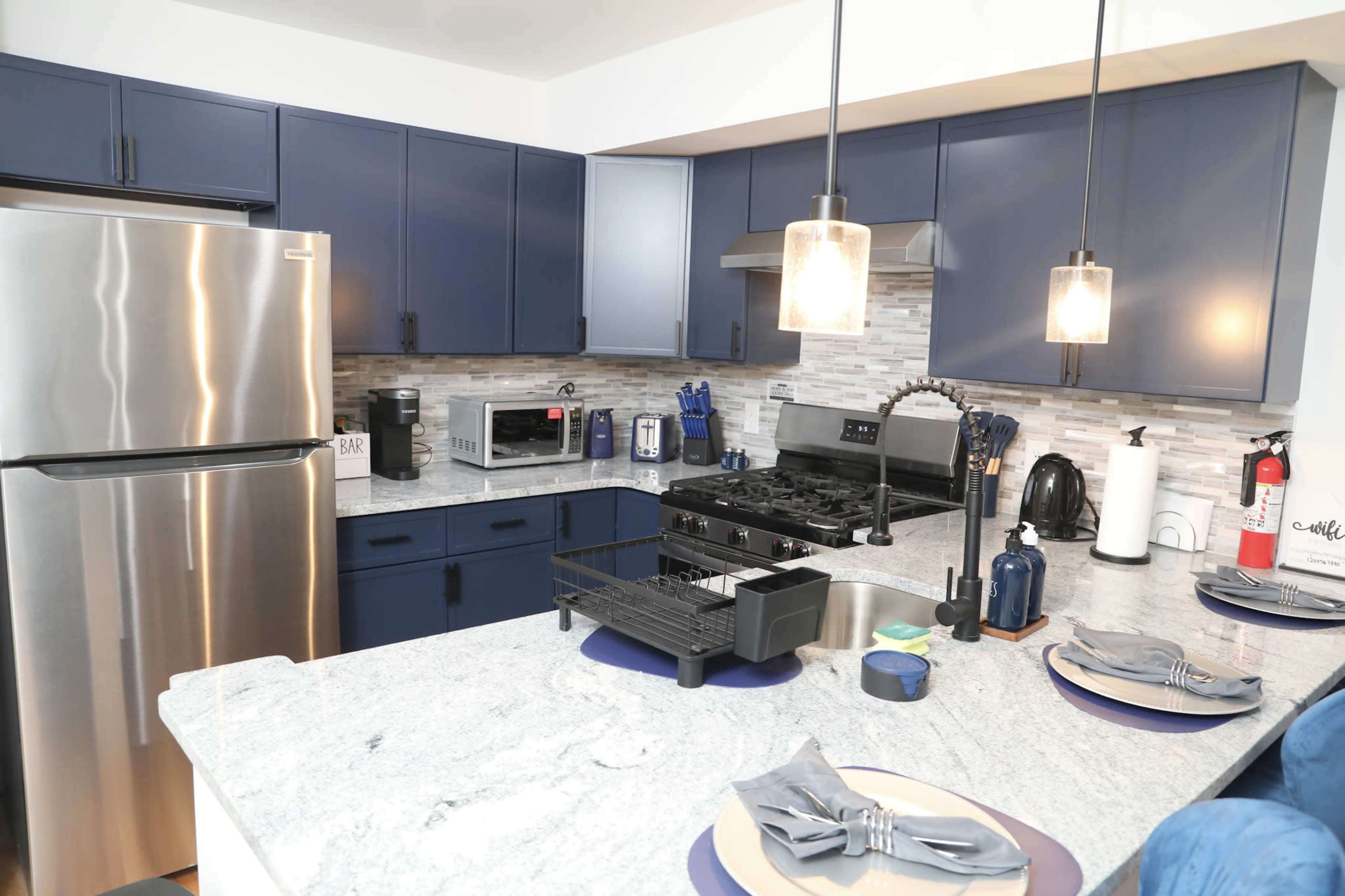 The image shows a modern kitchen with navy blue cabinets, stainless steel appliances, and a granite countertop, featuring a stove, microwave, and sink.
