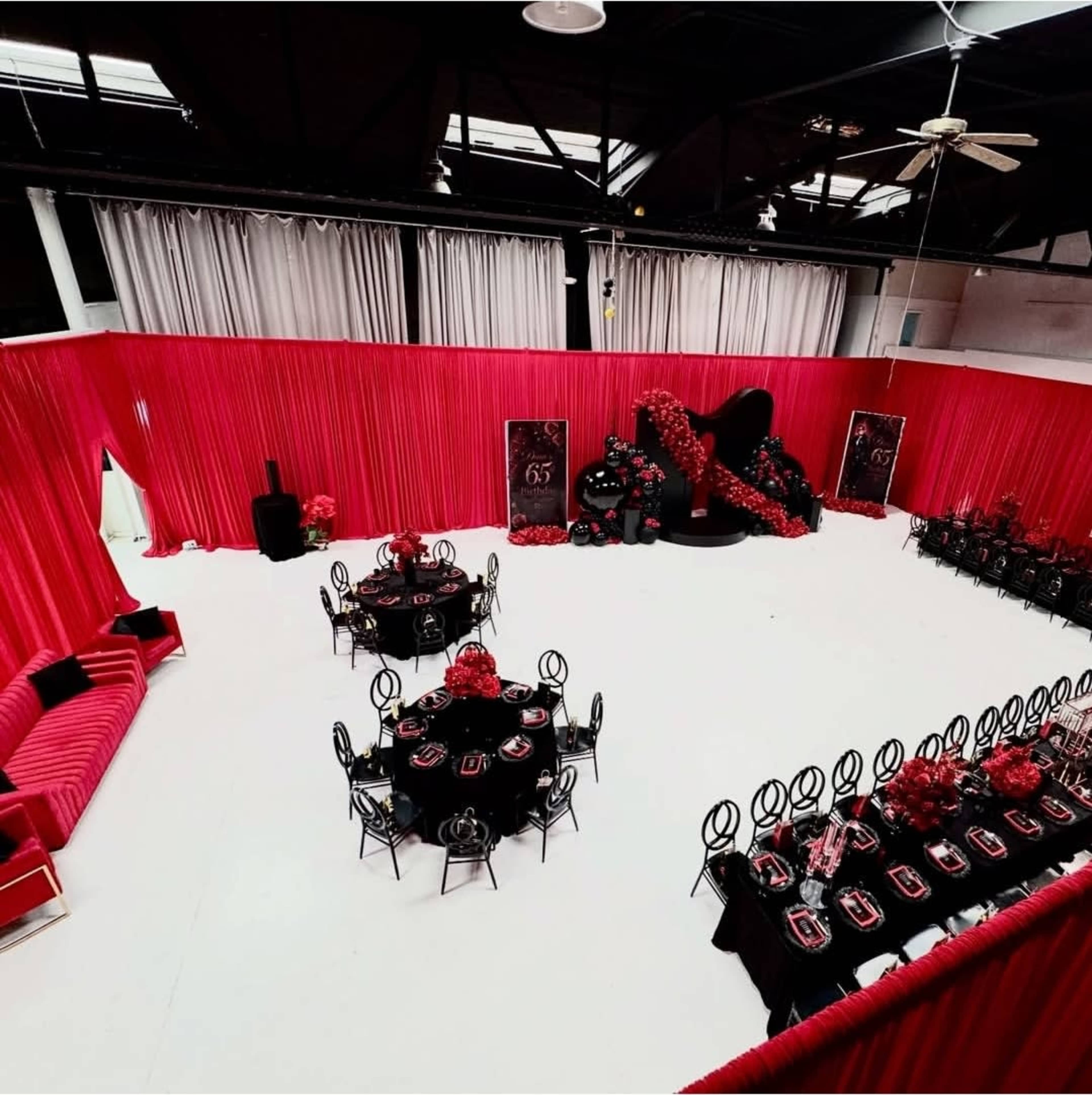 The image shows a spacious event venue decorated with red drapes, black furniture, and tables set for a formal gathering.