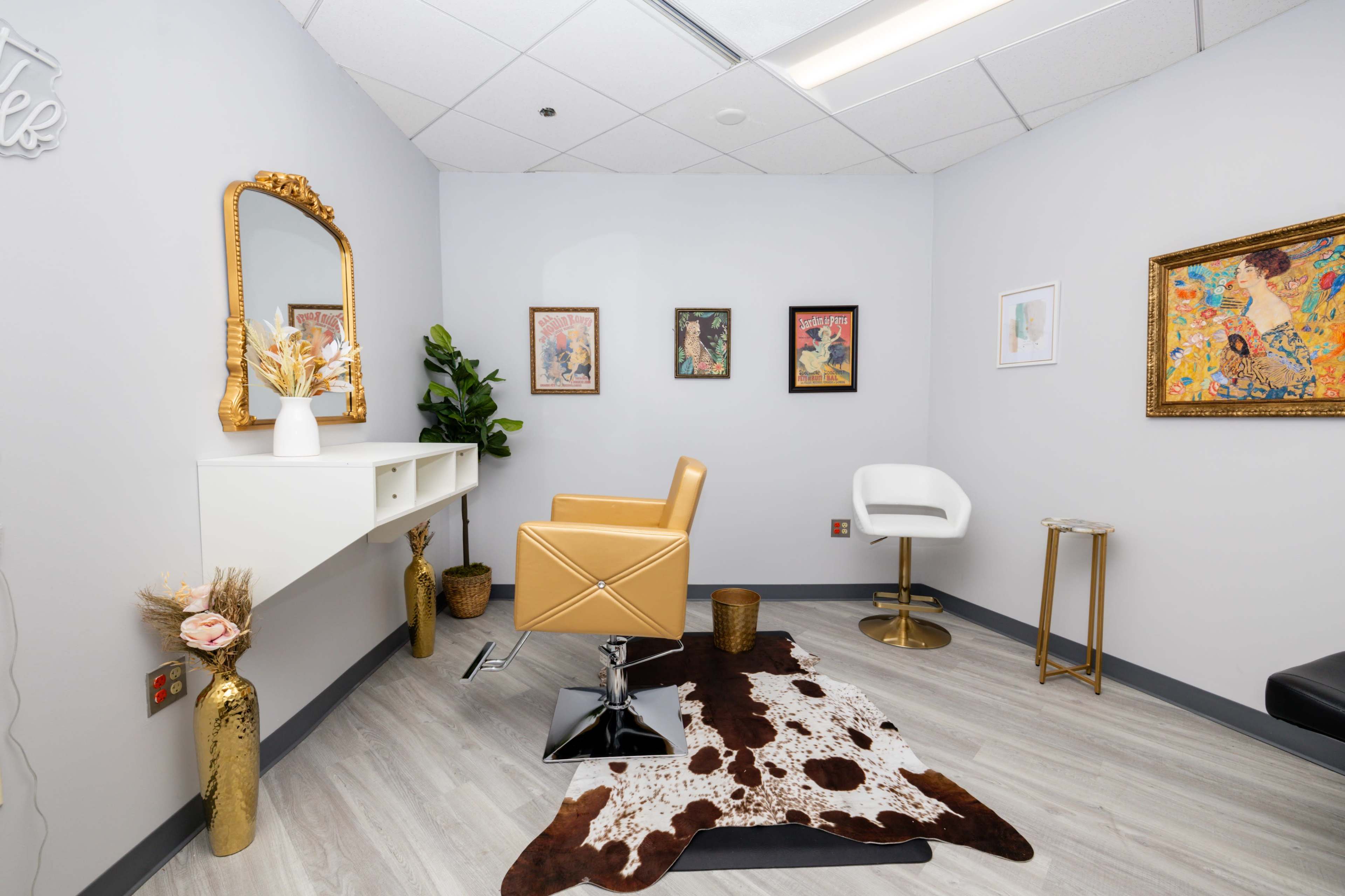 The image shows a modern interior space featuring a small vanity area with a mirror, an orange chair, two art pieces on the walls, and a cowhide rug on the floor.