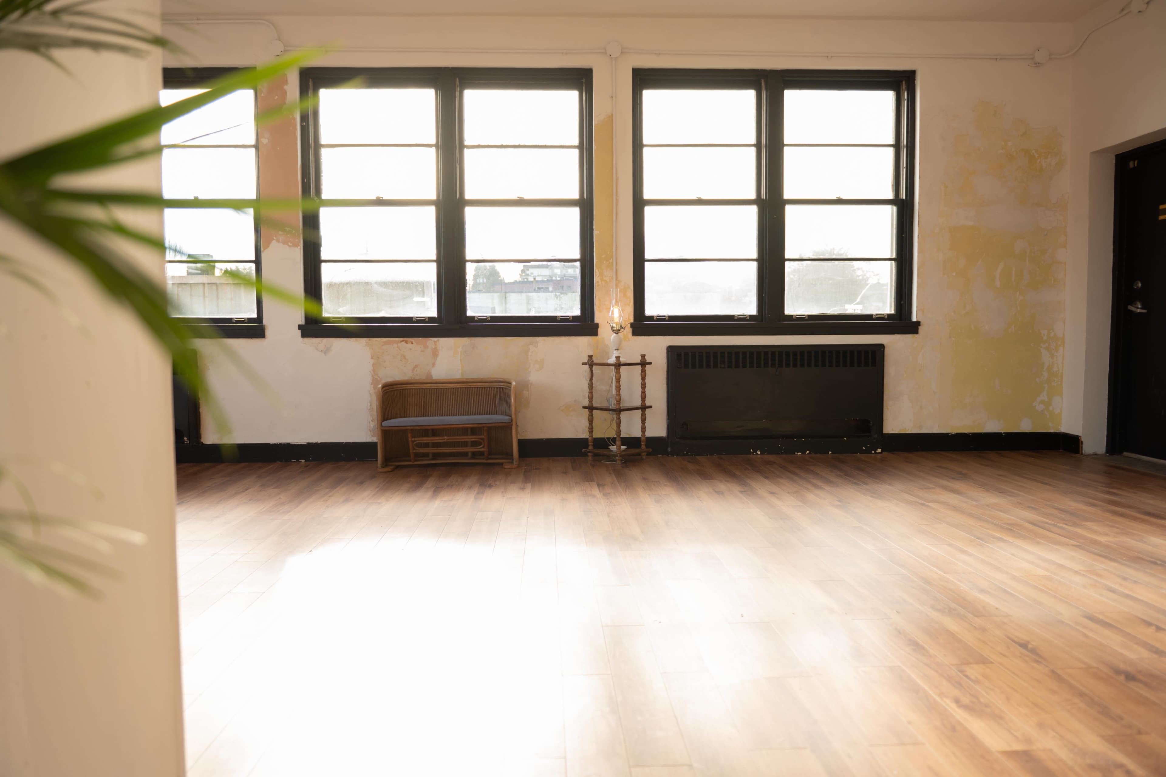 A spacious room with large windows, bare wooden floors, and peeling yellow paint on the walls.