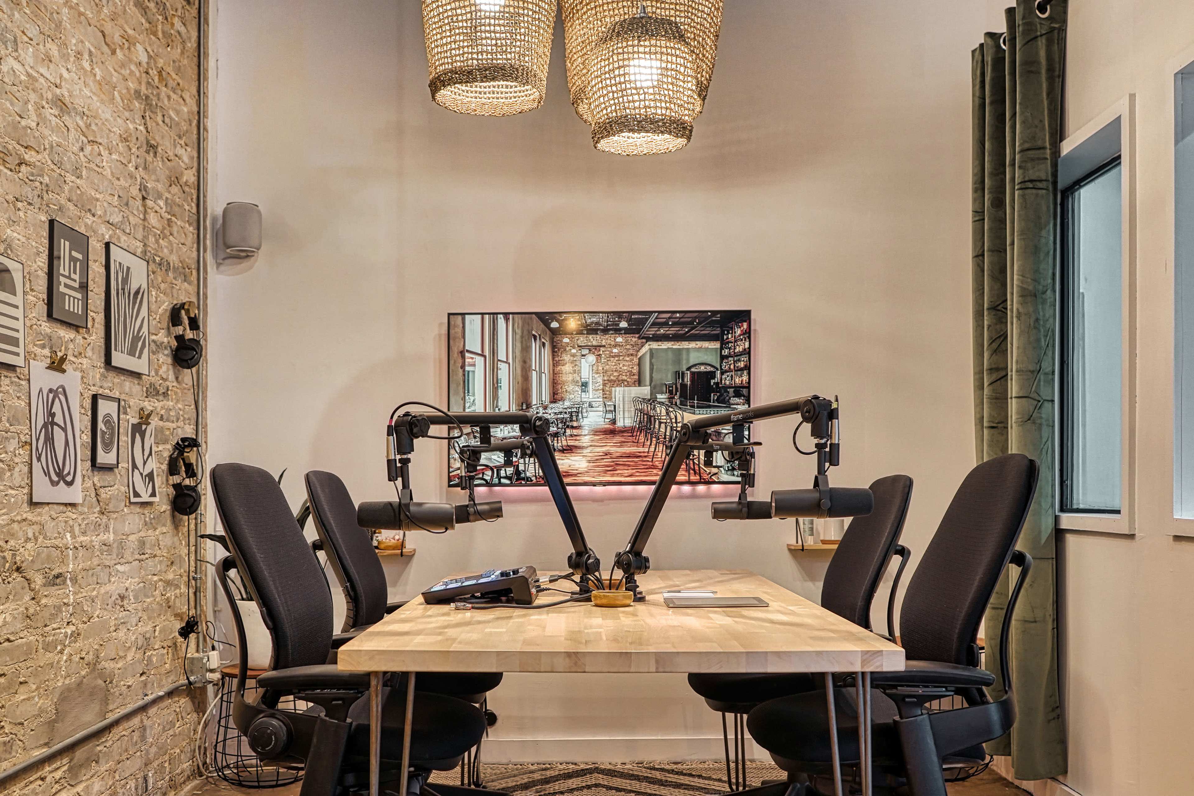 A modern conference room features a wooden table surrounded by ergonomic chairs and two microphone arms mounted on the table, with a brick wall and a decorative screen in the background.