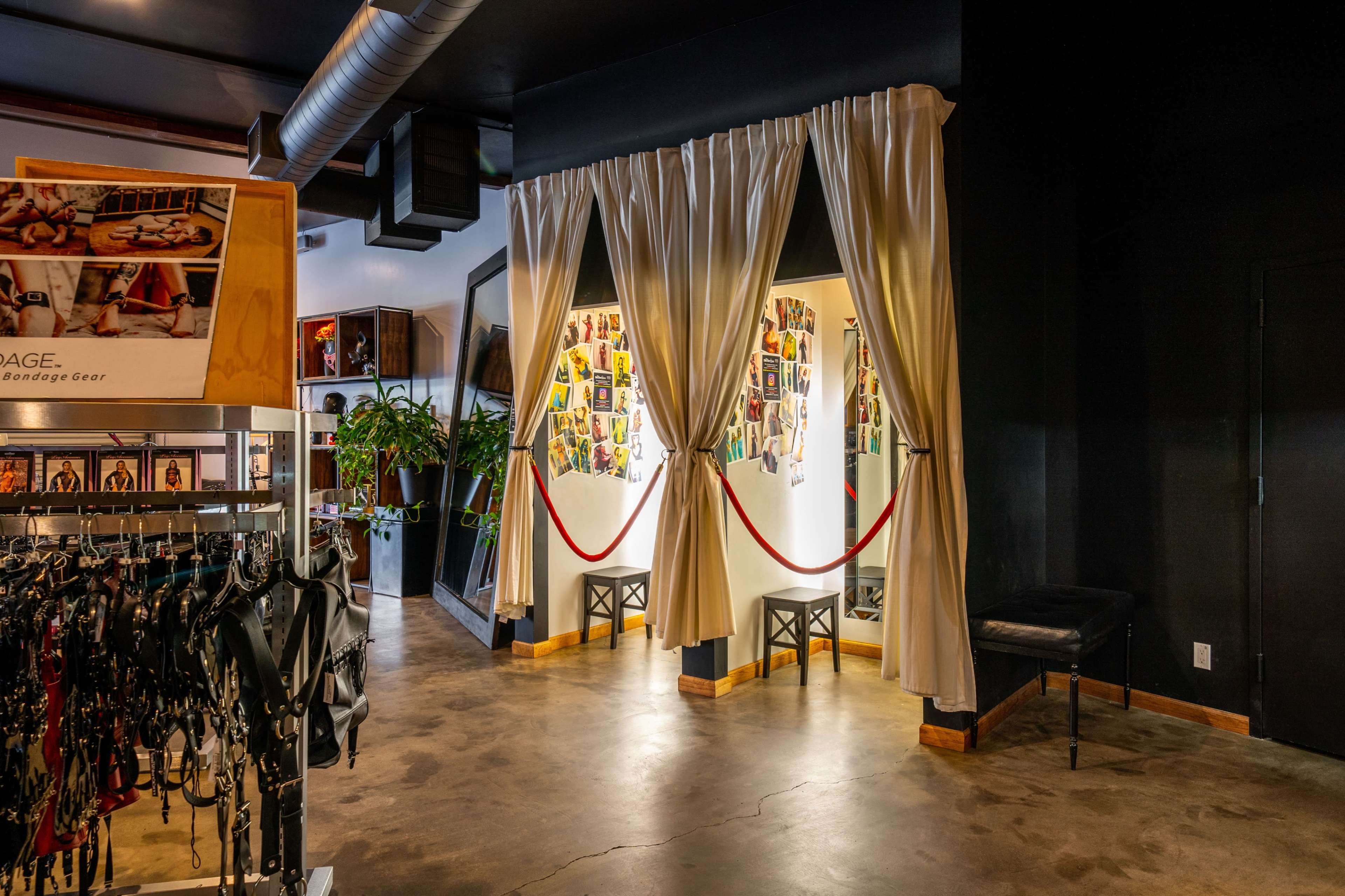 A dimly lit room with a display of bondage gear on racks, flanked by curtain-covered entrances and walls adorned with photographs.