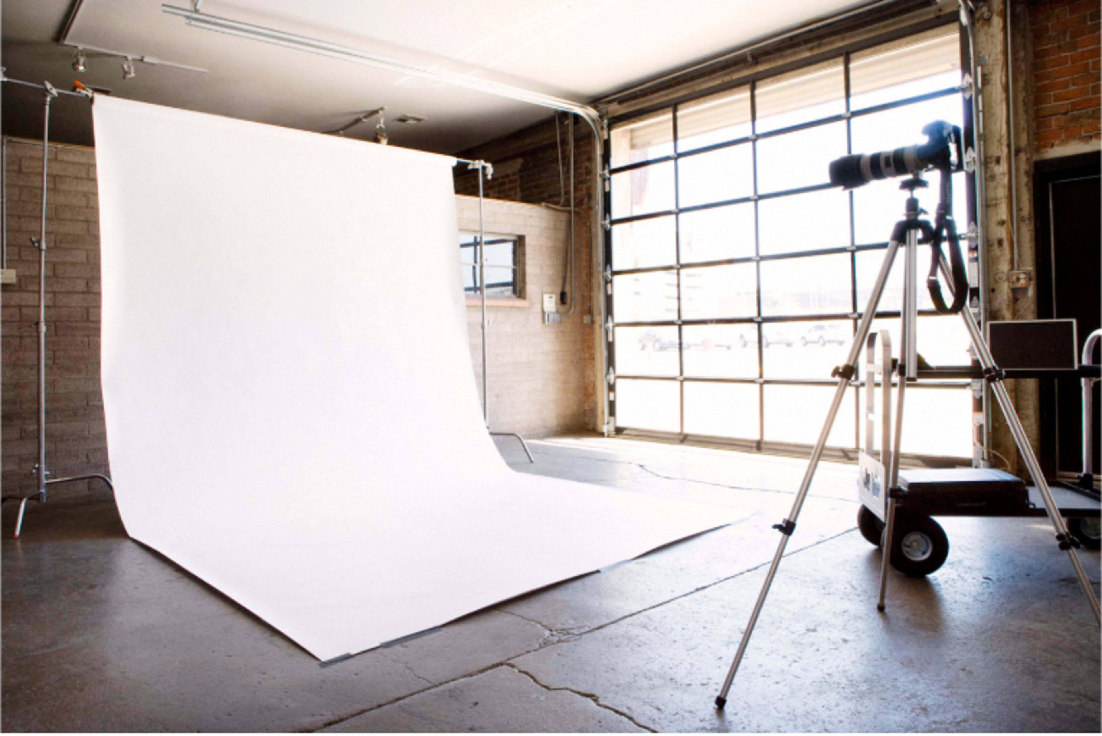A camera is set up in a studio with a white backdrop and large garage-style windows.