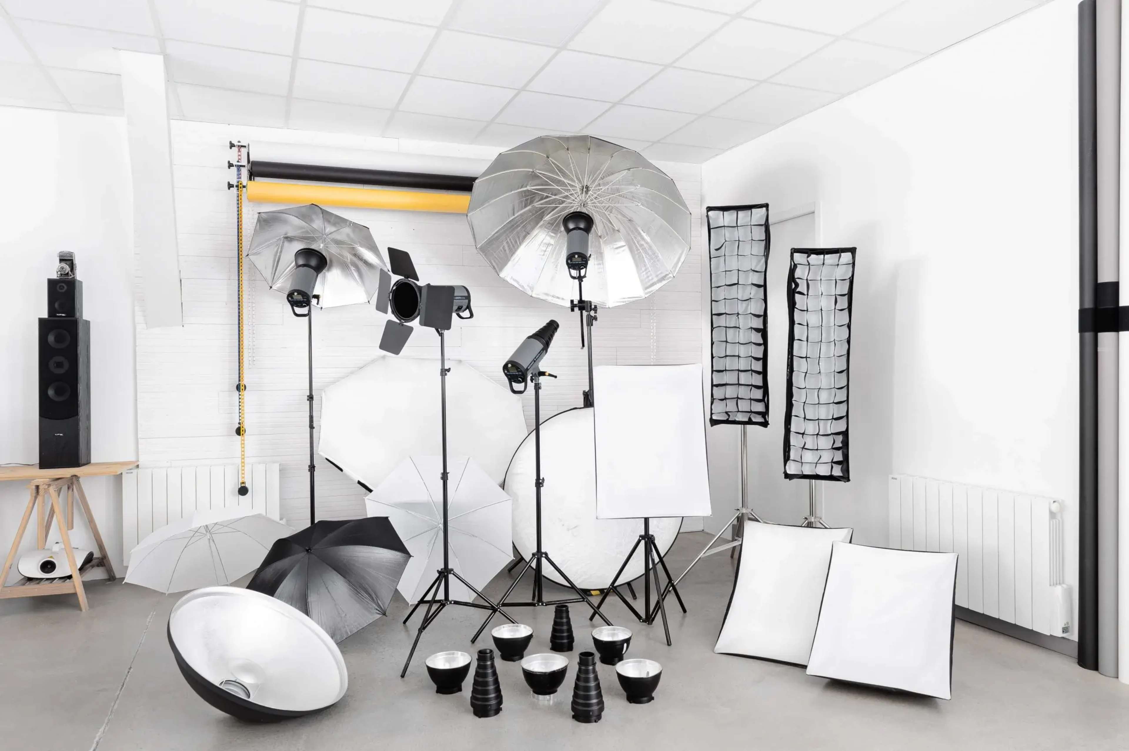 A photography studio is set up with various lighting equipment, reflectors, and umbrellas arranged neatly on the floor and stands.