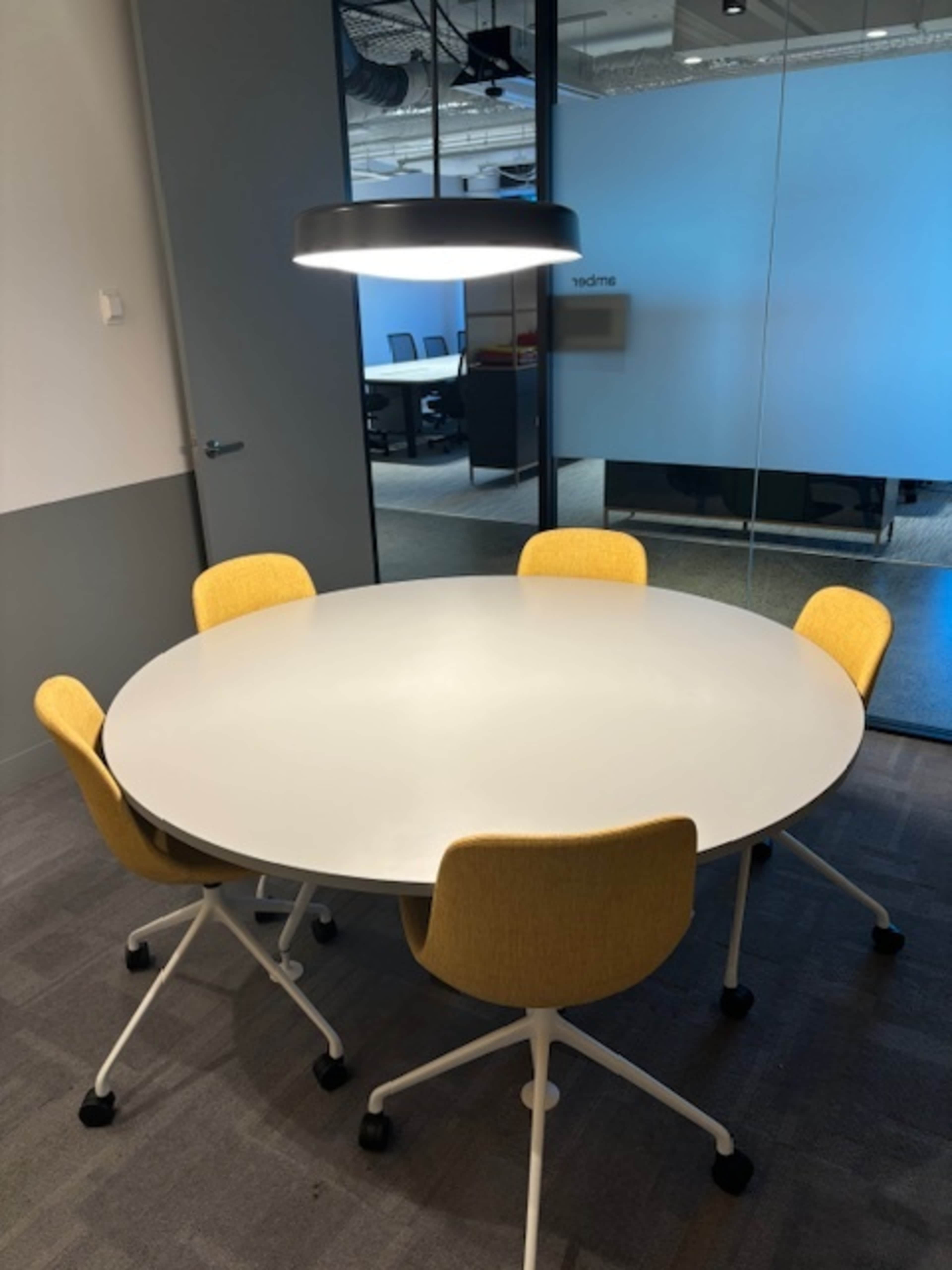 A round white table is surrounded by five yellow chairs in a modern conference room.