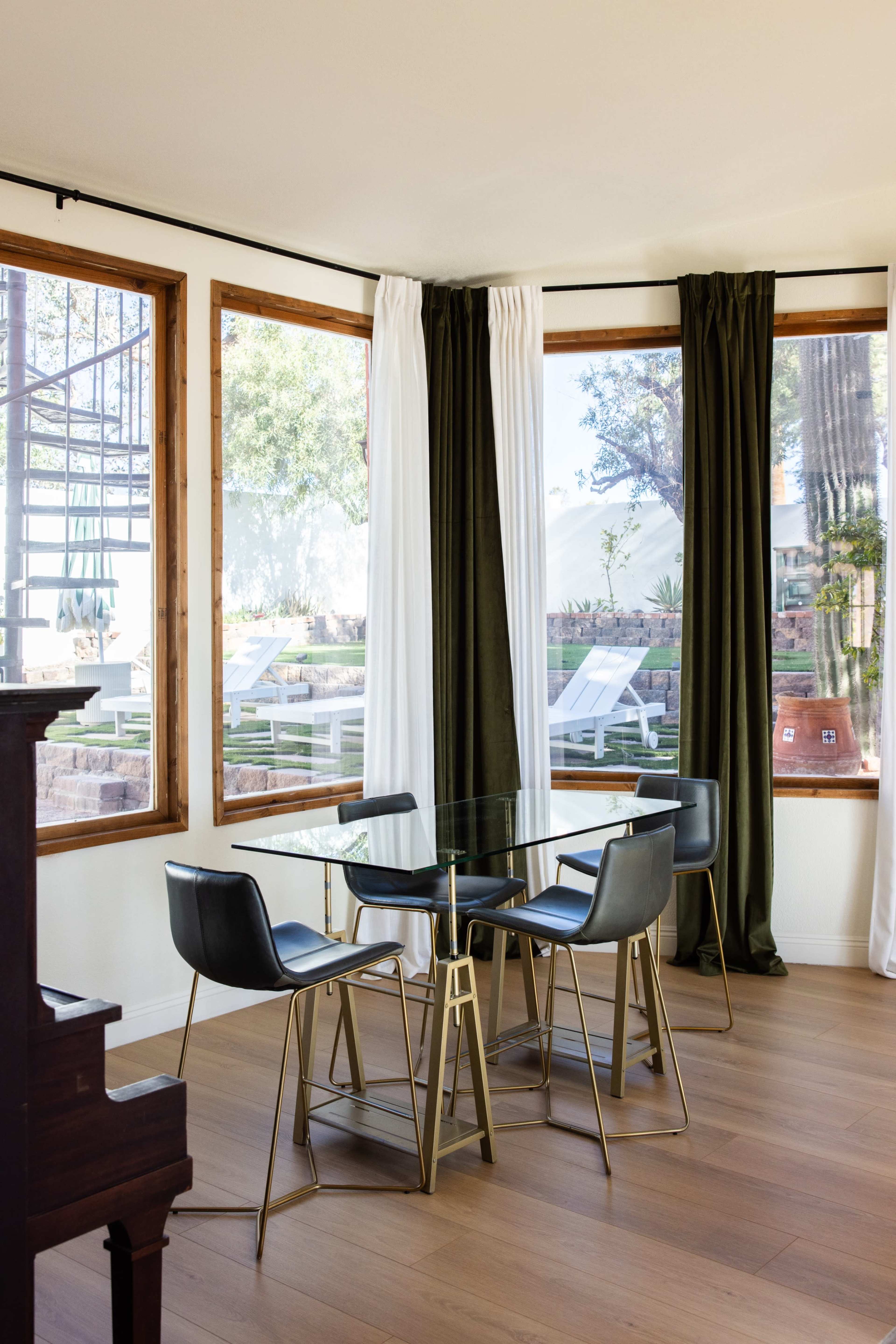 A modern dining area features a glass table surrounded by black chairs, with large windows and natural light illuminating the space.