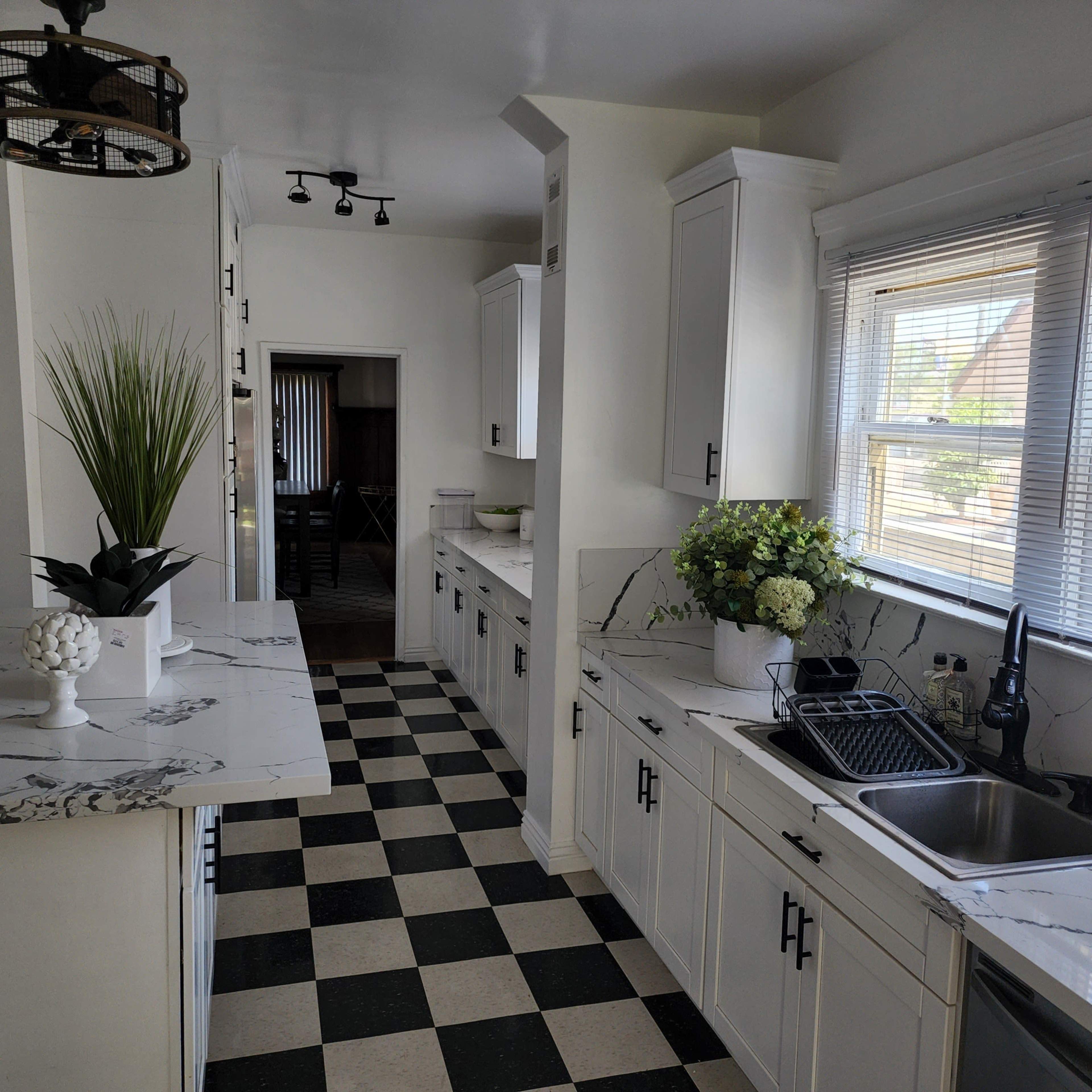 The image shows a modern kitchen with white cabinetry, a marble counter, and a black-and-white checkerboard floor.