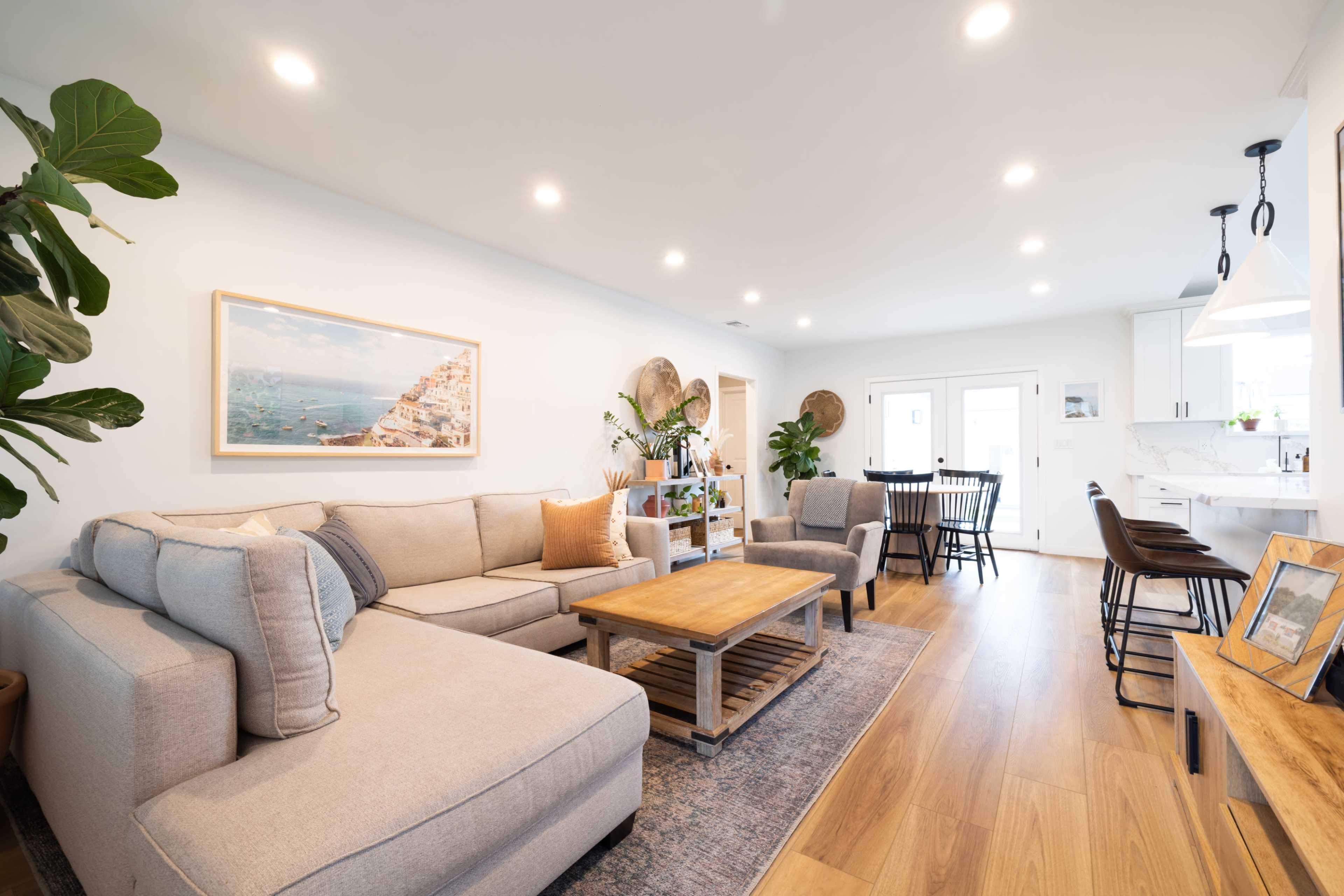 A light-filled living room features a sectional sofa, a wooden coffee table, and an adjacent dining area with a round table and chairs.