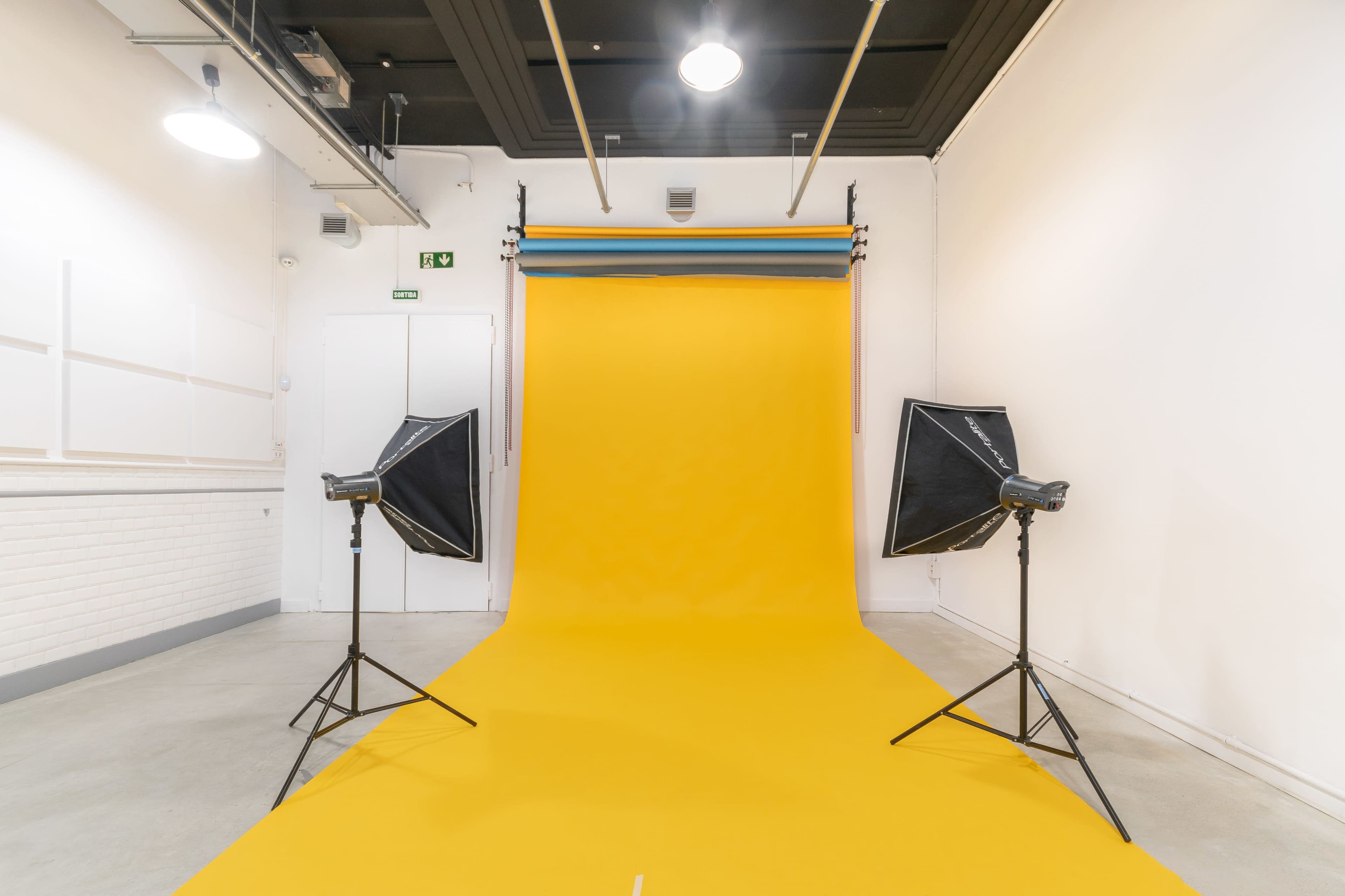A photography studio with a vibrant yellow backdrop and two softbox lights positioned on either side.
