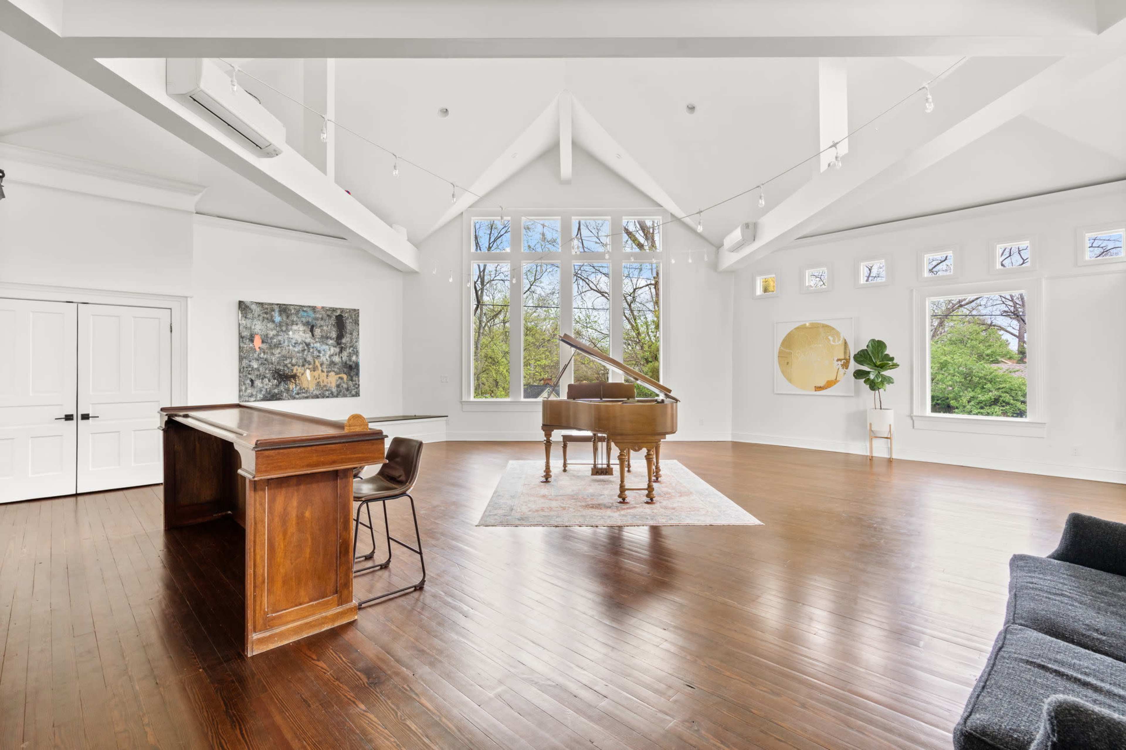The spacious room features a grand piano at its center, surrounded by large windows that invite natural light.