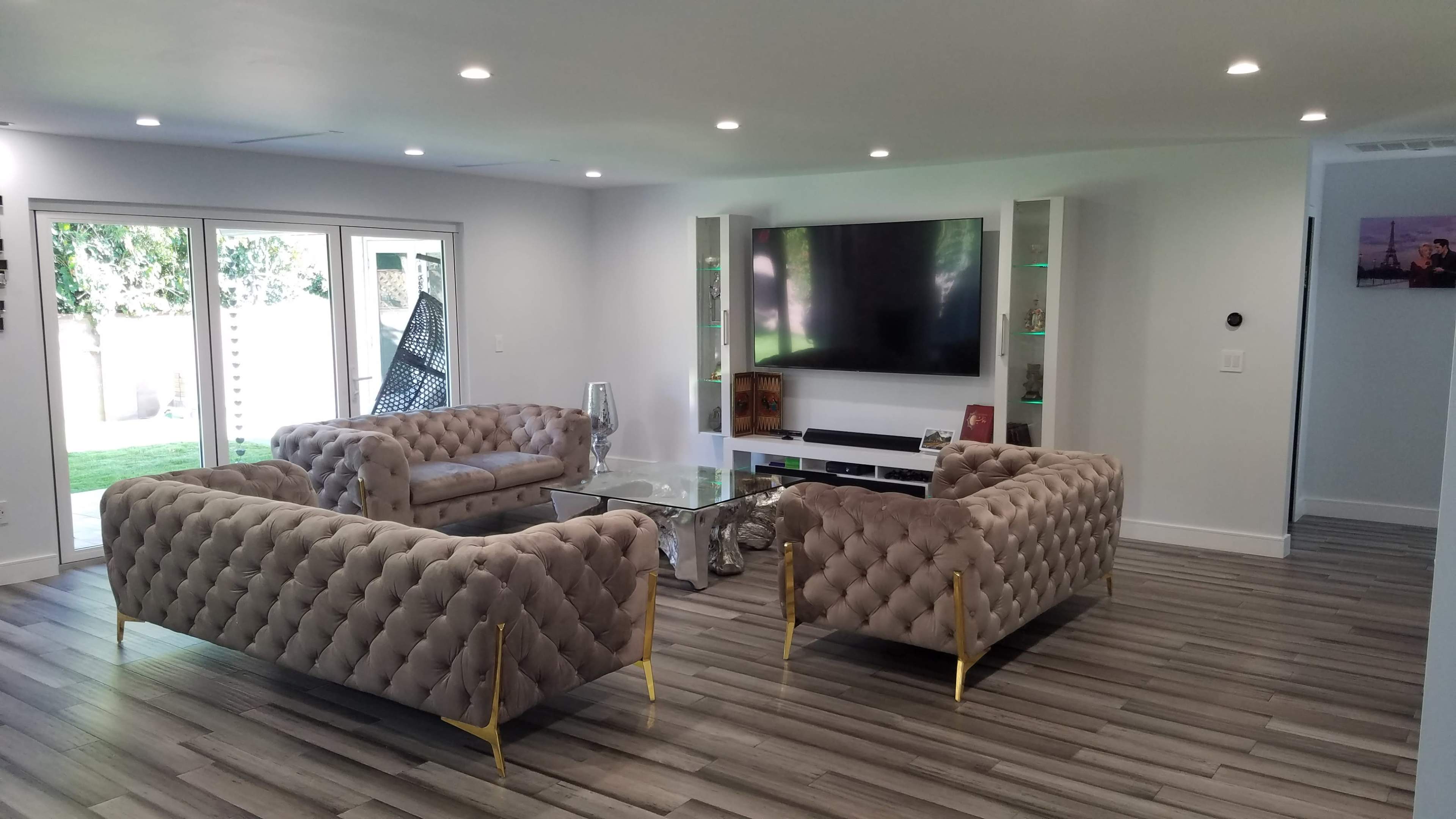 A modern living room with two tufted sofas facing each other, a glass coffee table in the center, and a large television mounted on the wall above a media console.