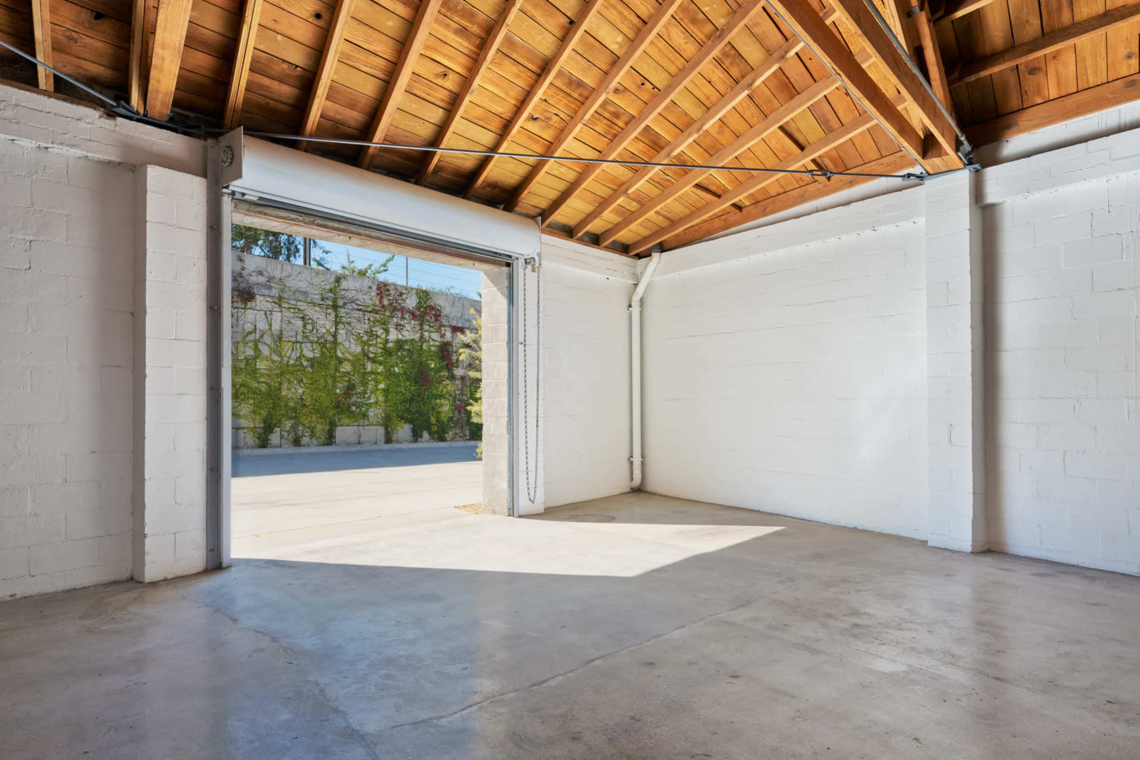 The image shows an empty room with white walls, a concrete floor, and a large open doorway leading to an exterior space.