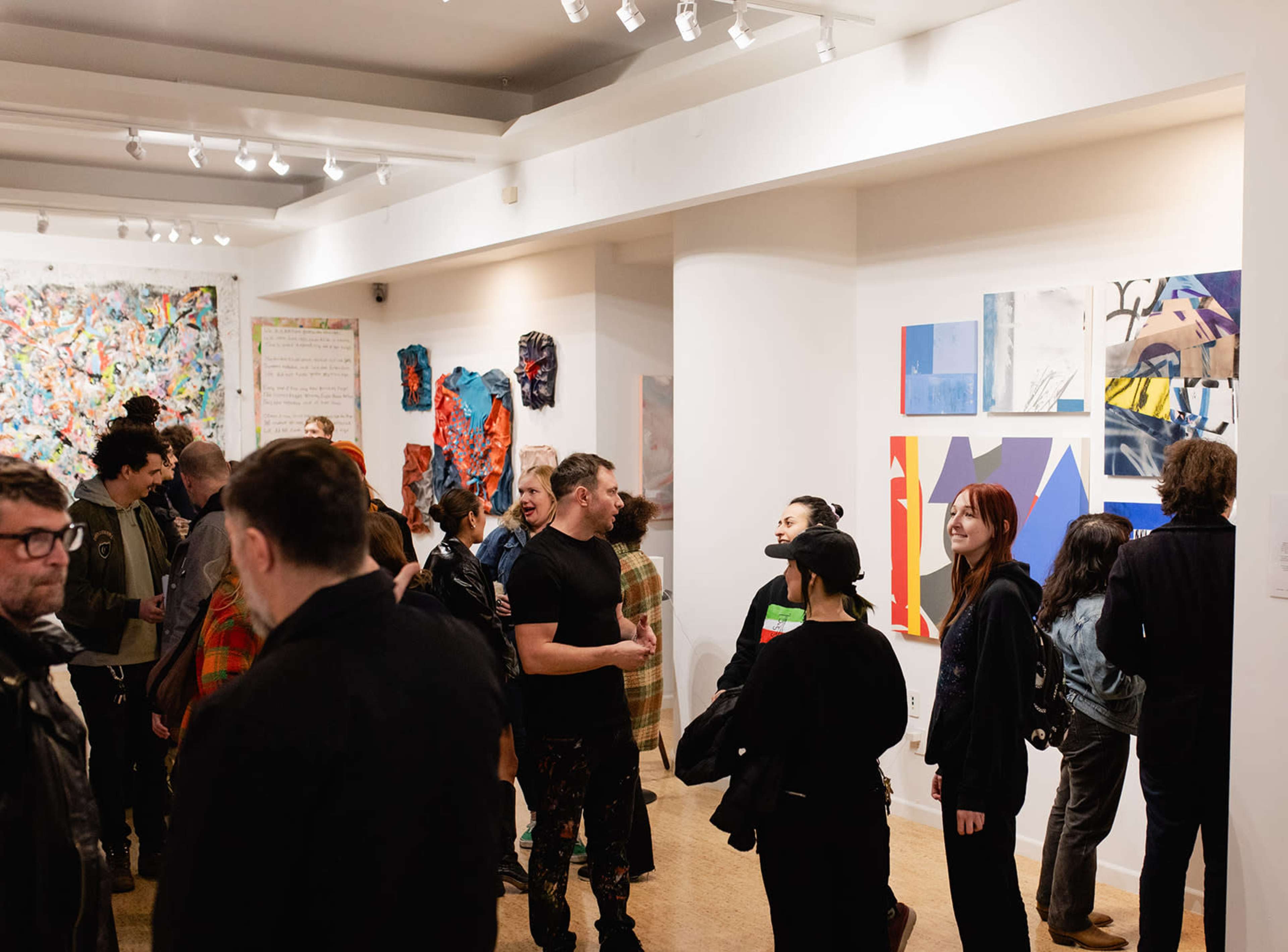A diverse group of people gathers in an art gallery surrounded by abstract paintings and colorful artworks.
