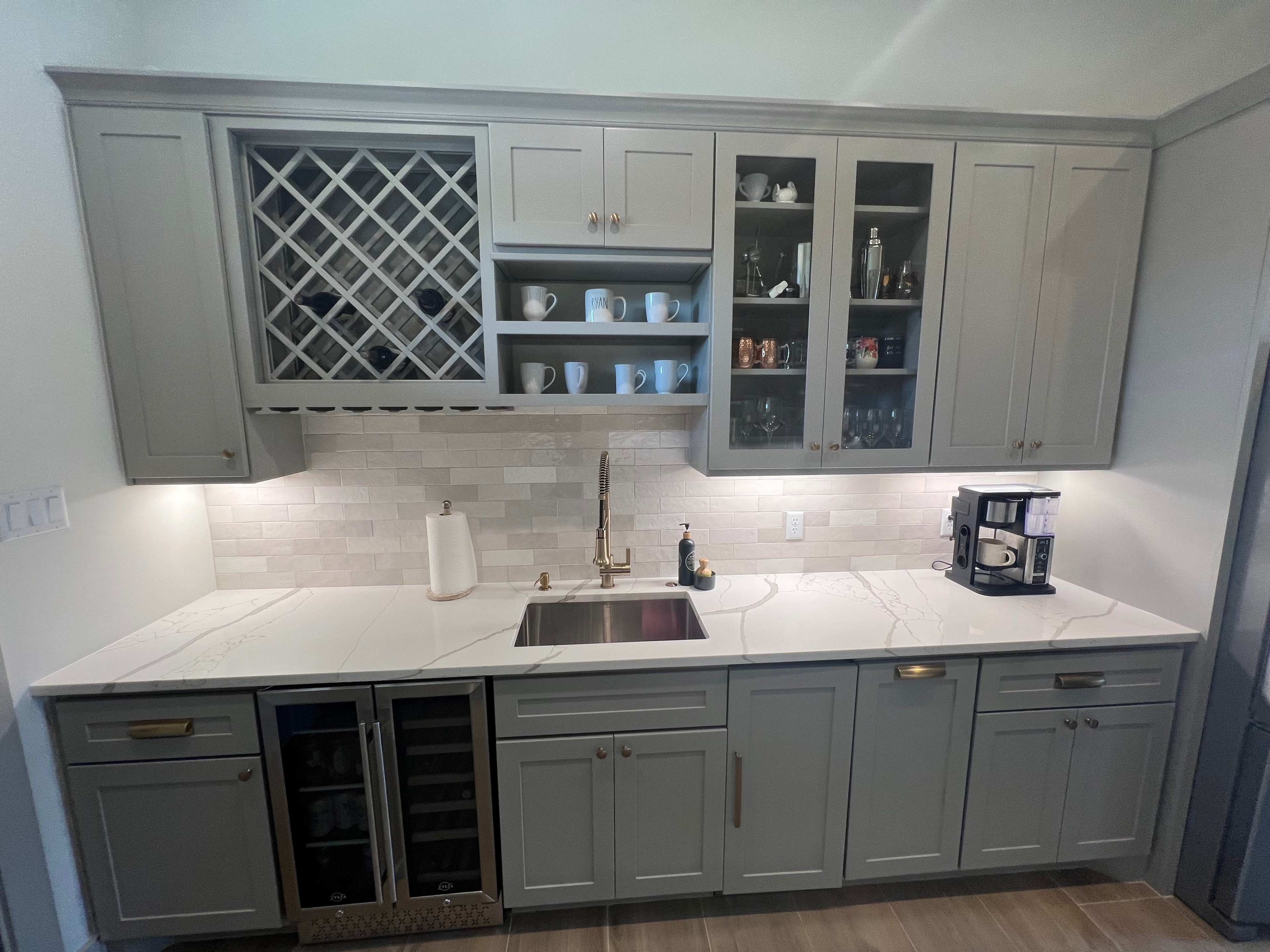 A modern kitchen with gray cabinetry, a sink, a wine rack, and a coffee maker on the countertop.