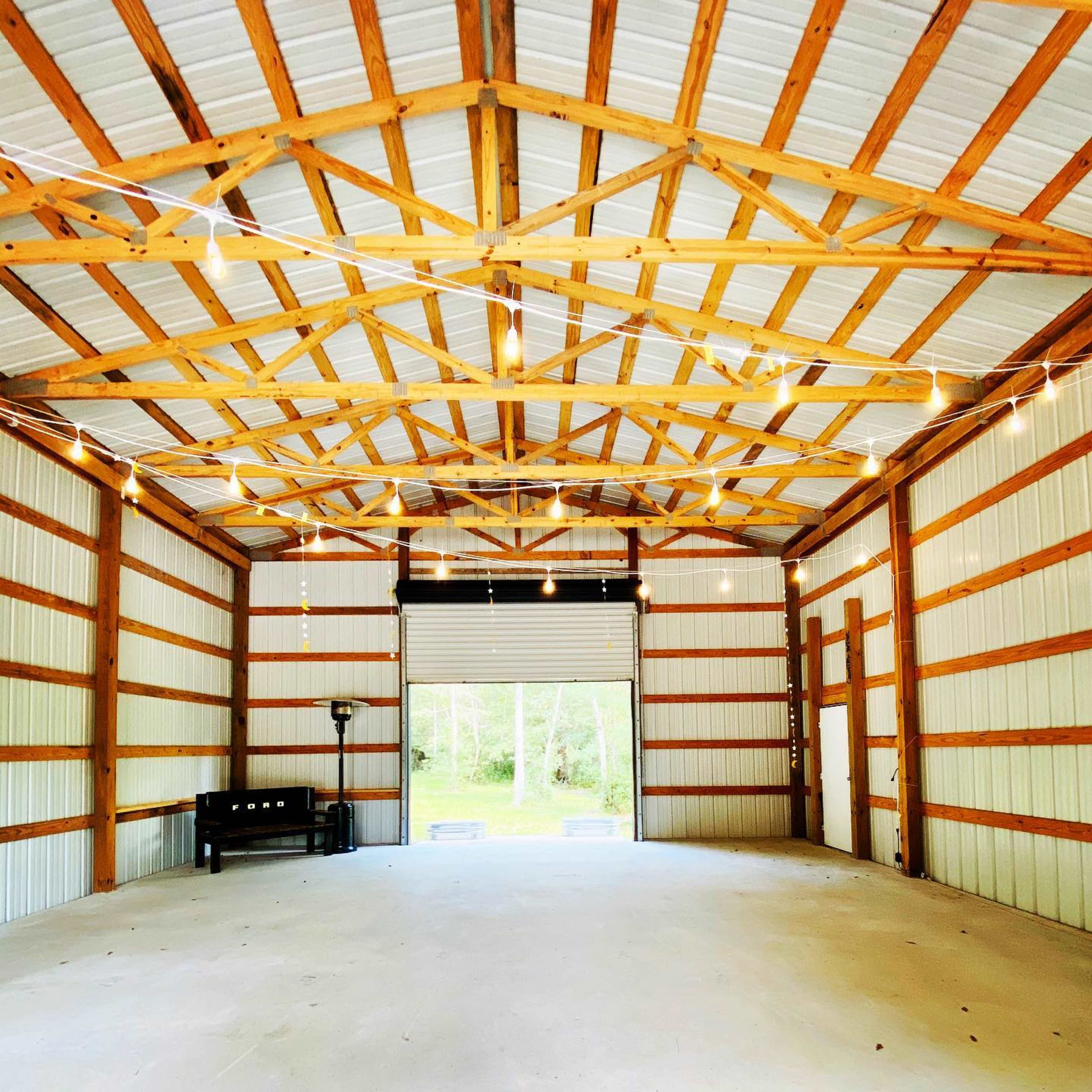 A spacious, empty barn interior with wooden beams and string lights hanging from the ceiling.