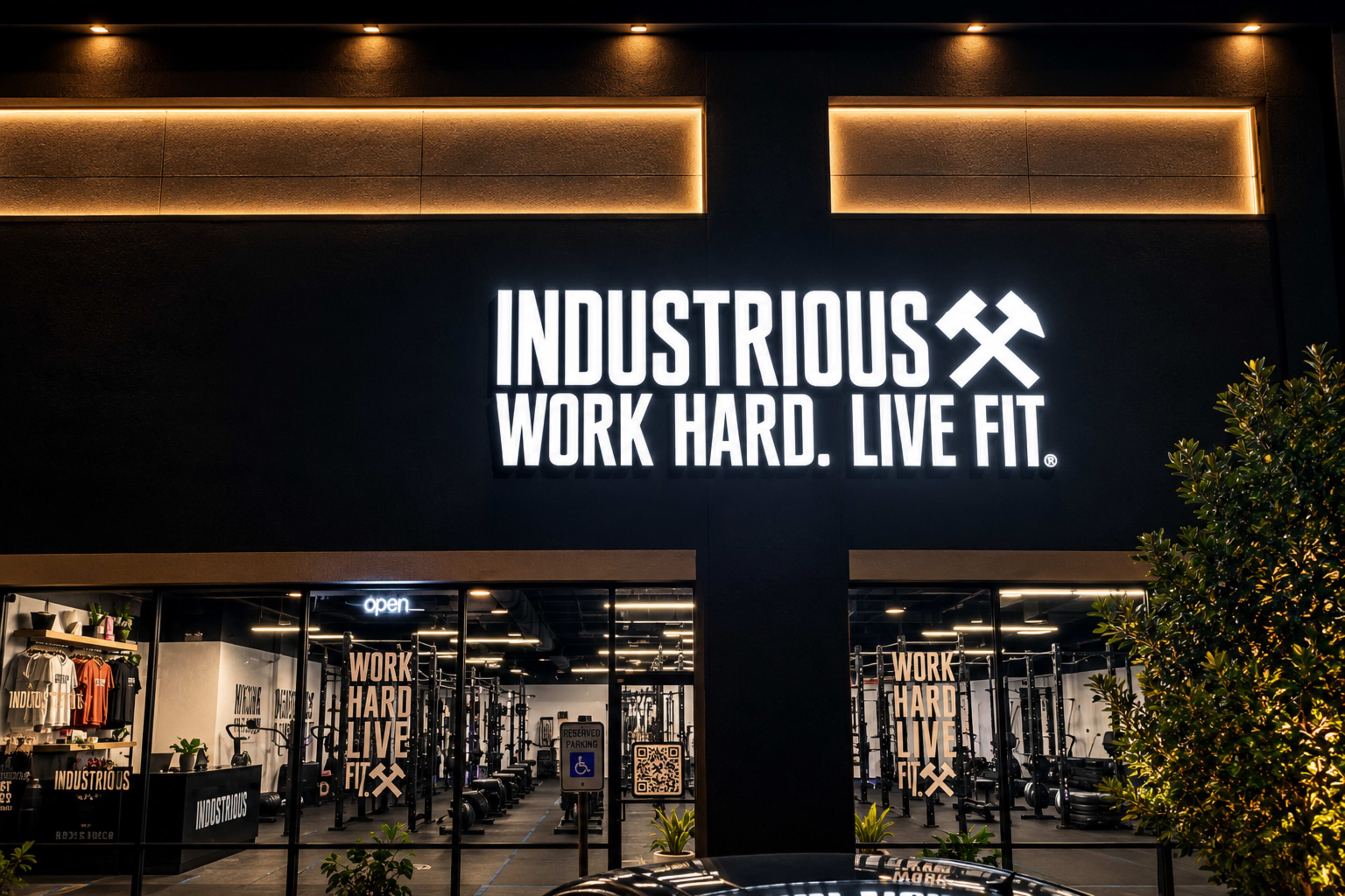 The image shows the exterior of a gym named "Industrious" with a sign that reads "WORK HARD. LIVE FIT." illuminated at night.