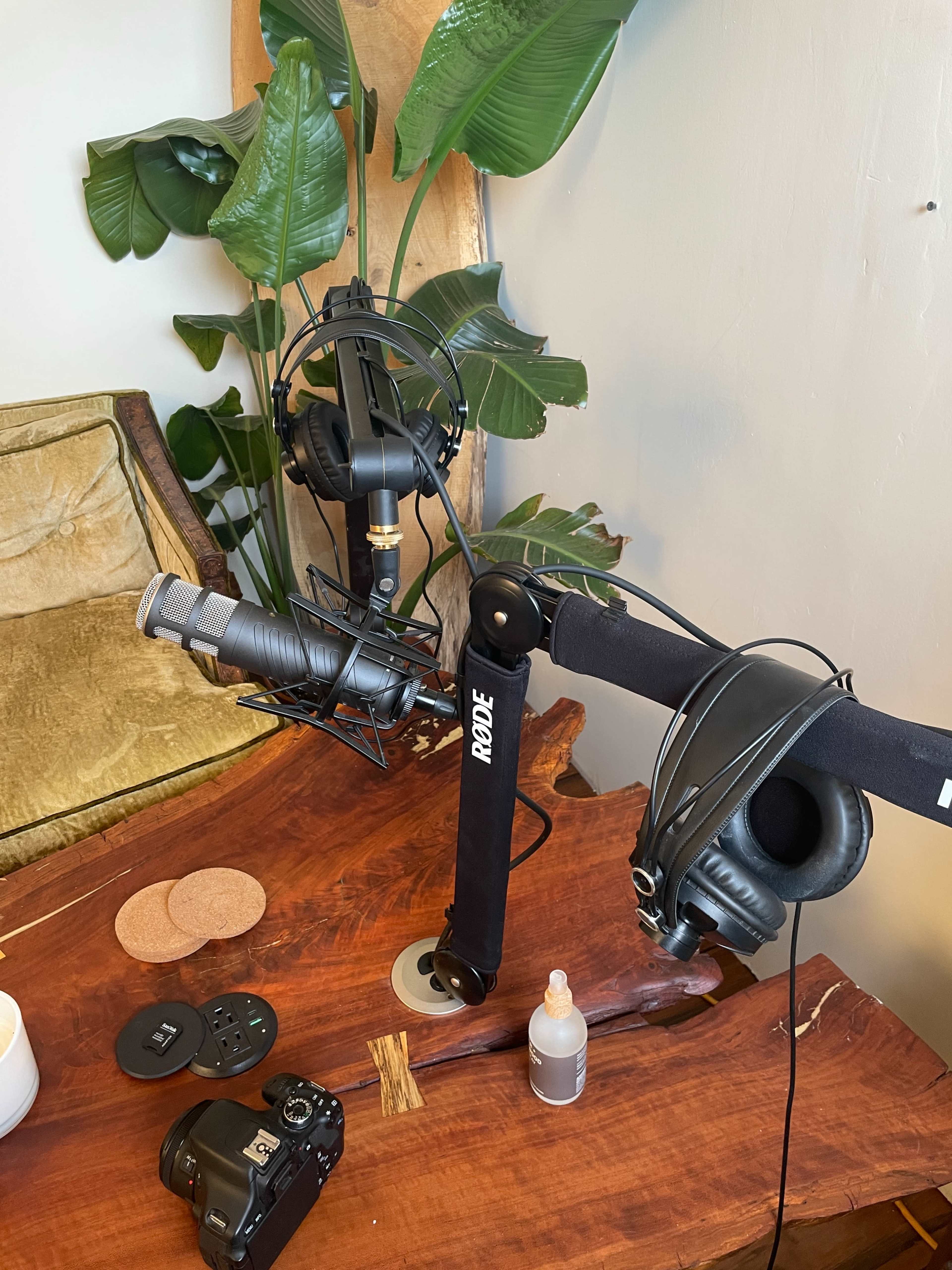 The image shows a wooden table with a microphone and headphones mounted on adjustable arms, along with a camera and other equipment nearby.