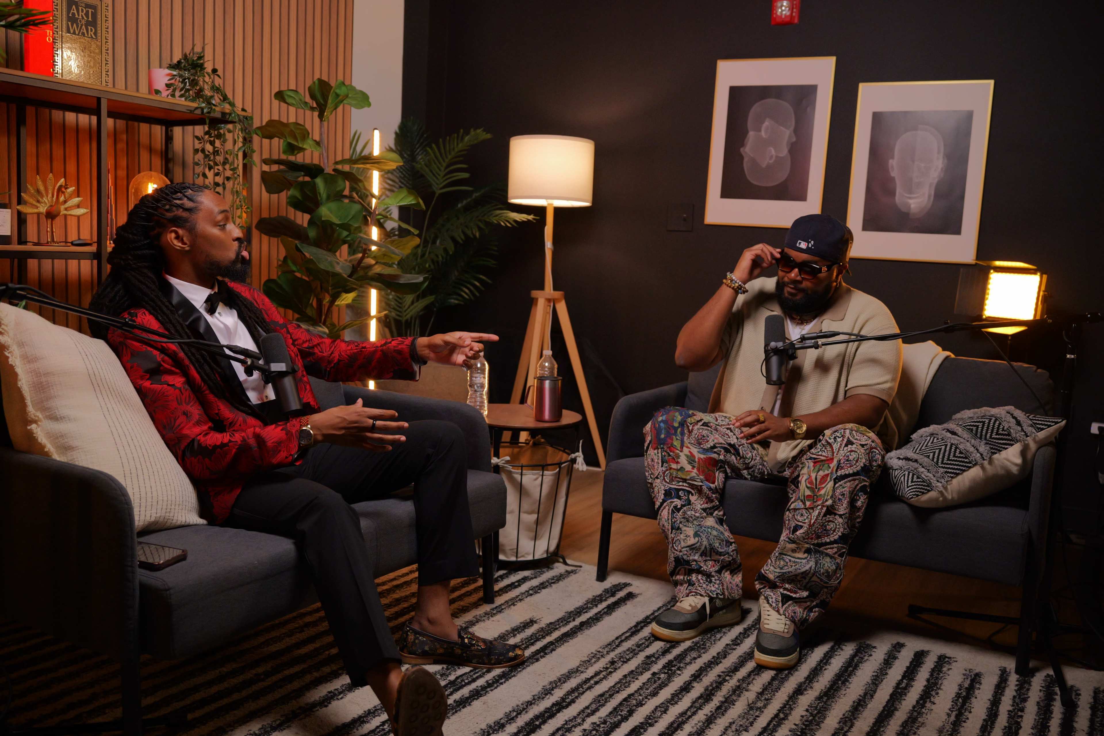 Two men are engaged in a conversation while seated on a pair of sofas in a modern, well-decorated room with plants and artwork.