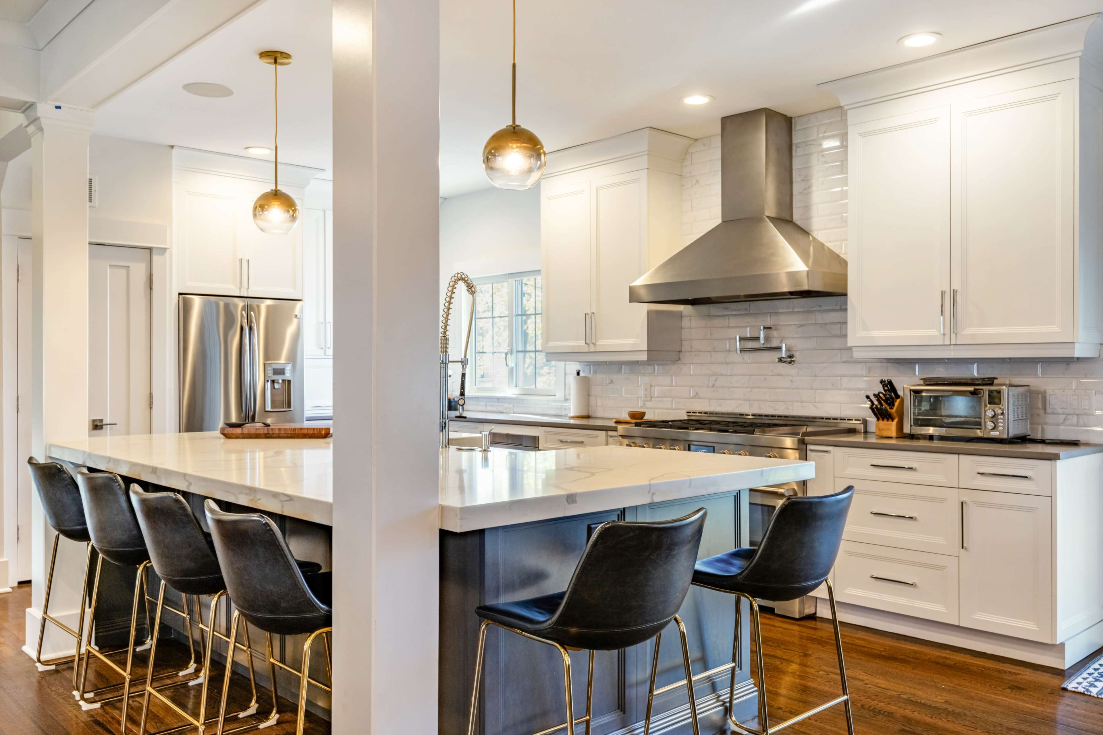 The image shows a modern kitchen featuring a large island with bar seating, stainless steel appliances, and white cabinetry.