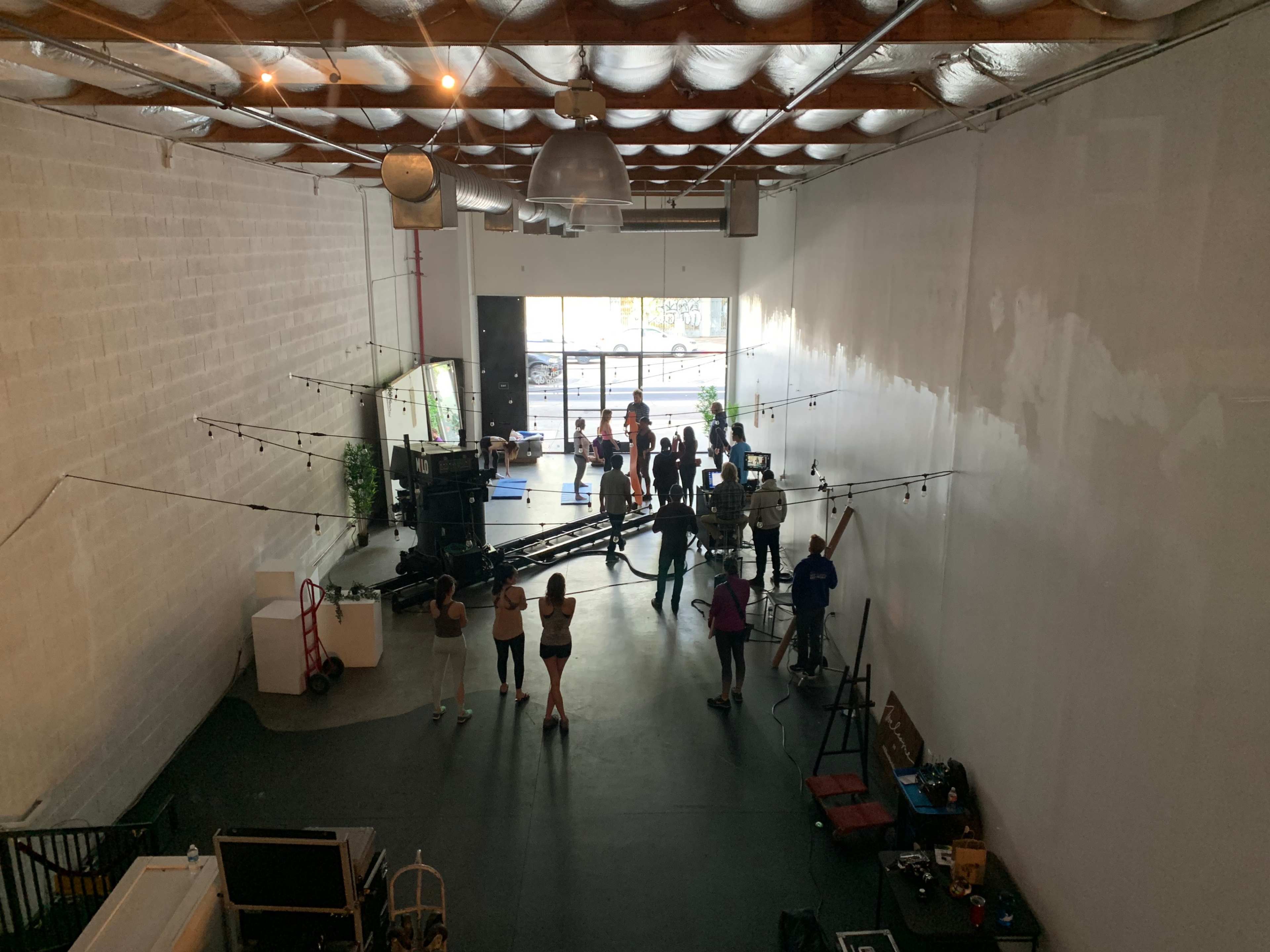 A group of people gathers on the floor of a large, open studio space with string lights and equipment set up for an event or production.