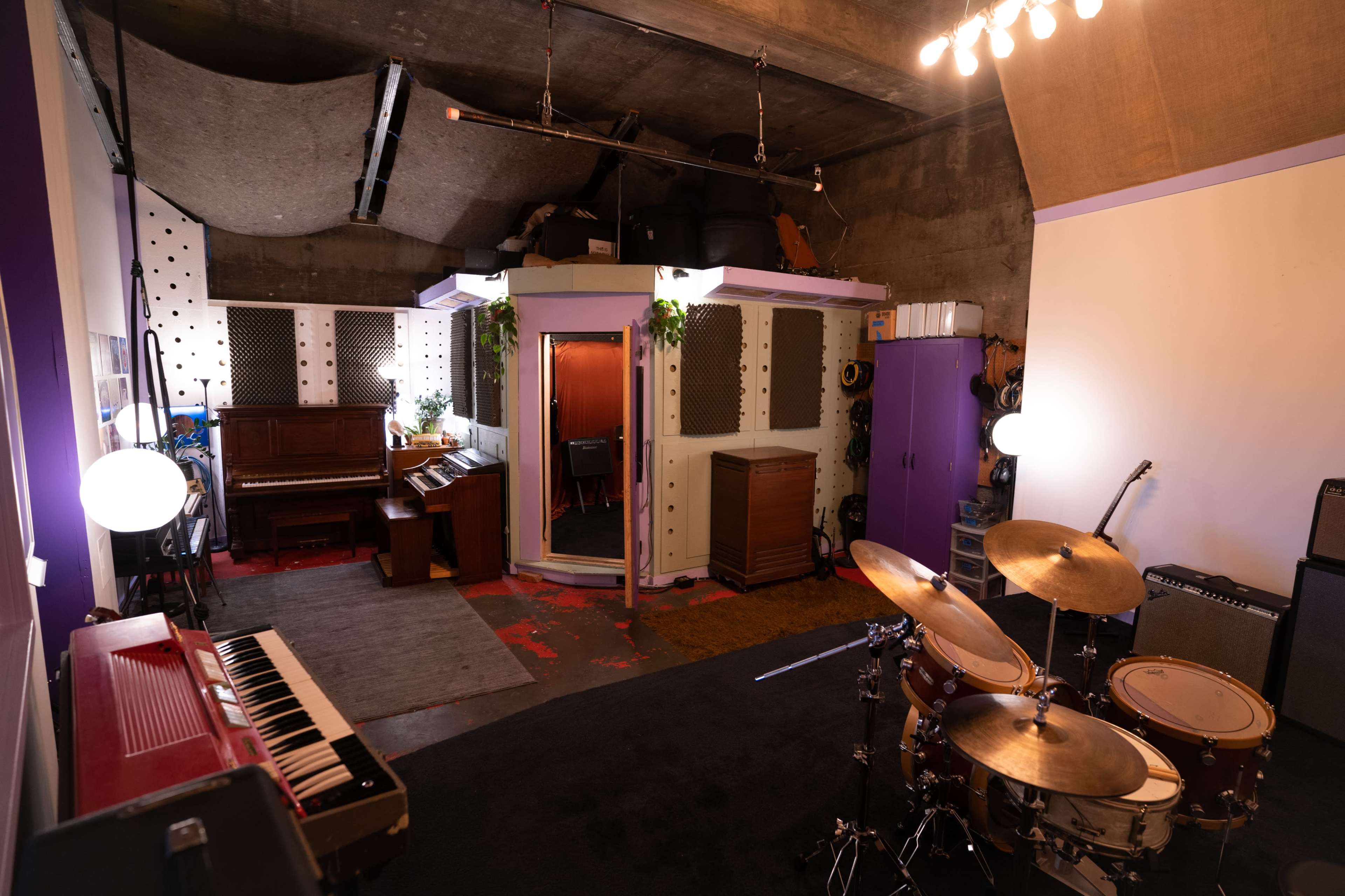 A recording studio with a drum set, a piano, and soundproofing panels on the walls.