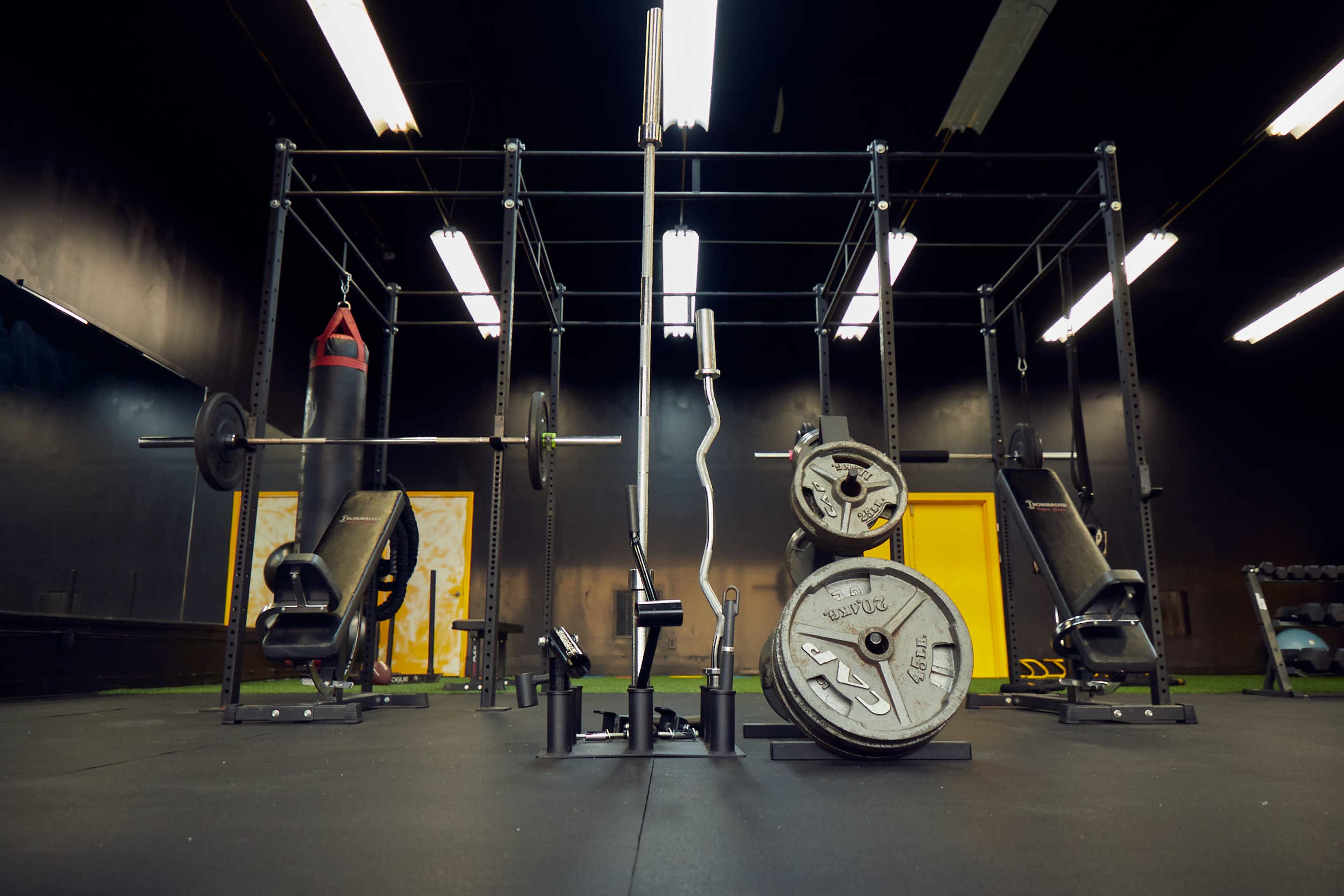 A gym facility with various strength training equipment, including weights and a punching bag, under overhead lights.