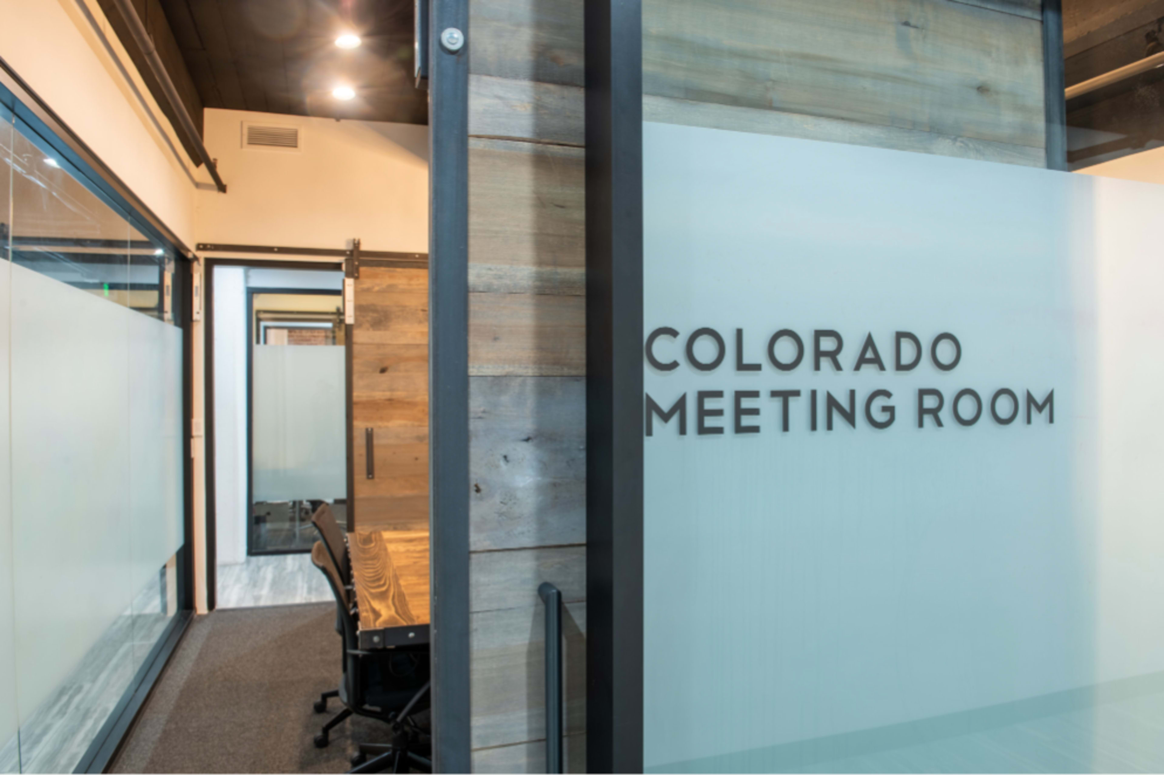 A glass wall with the words "COLORADO MEETING ROOM" features a wooden interior with chairs visible in the background.
