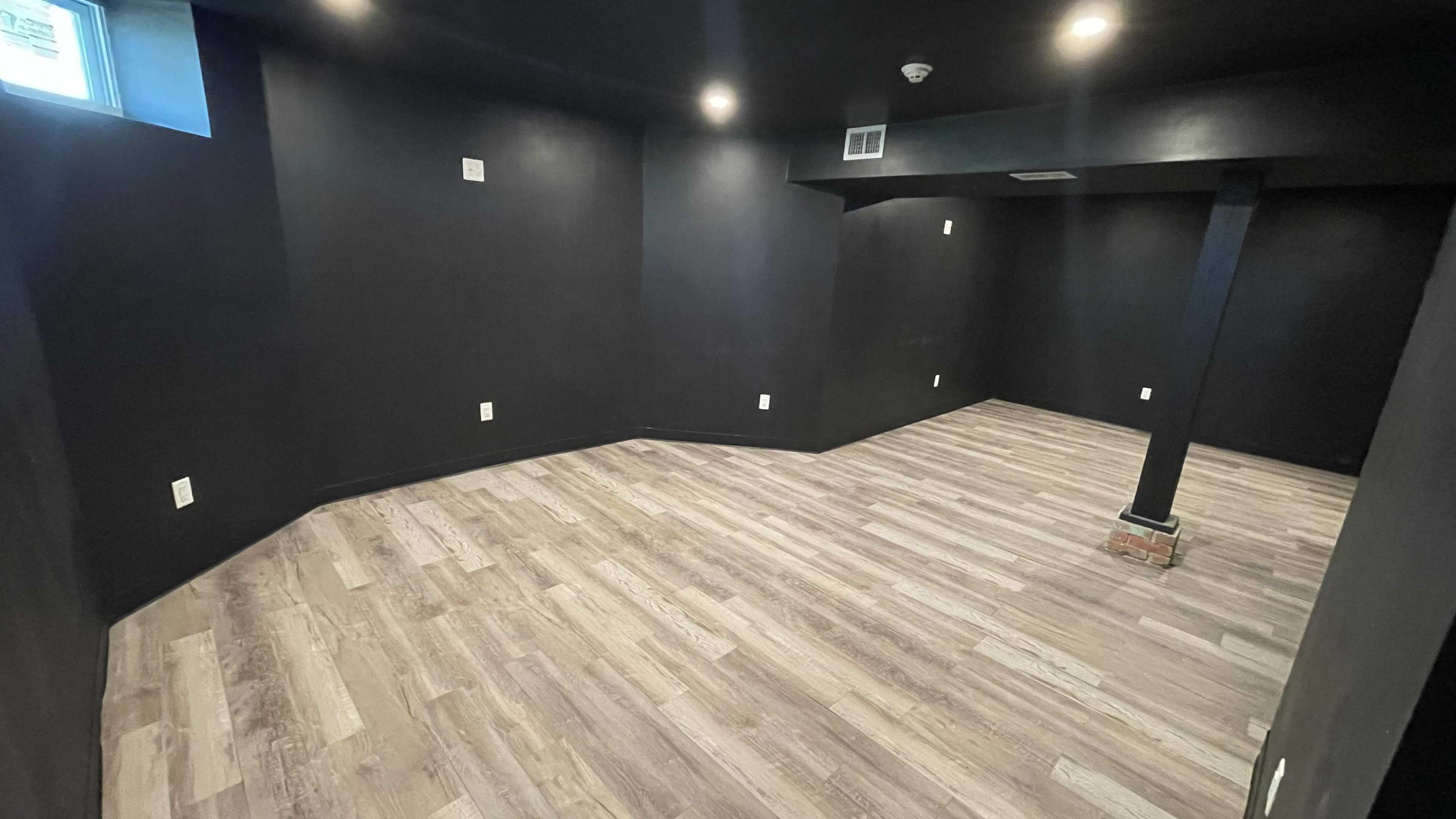 The image shows an empty room with black walls and light-colored flooring.