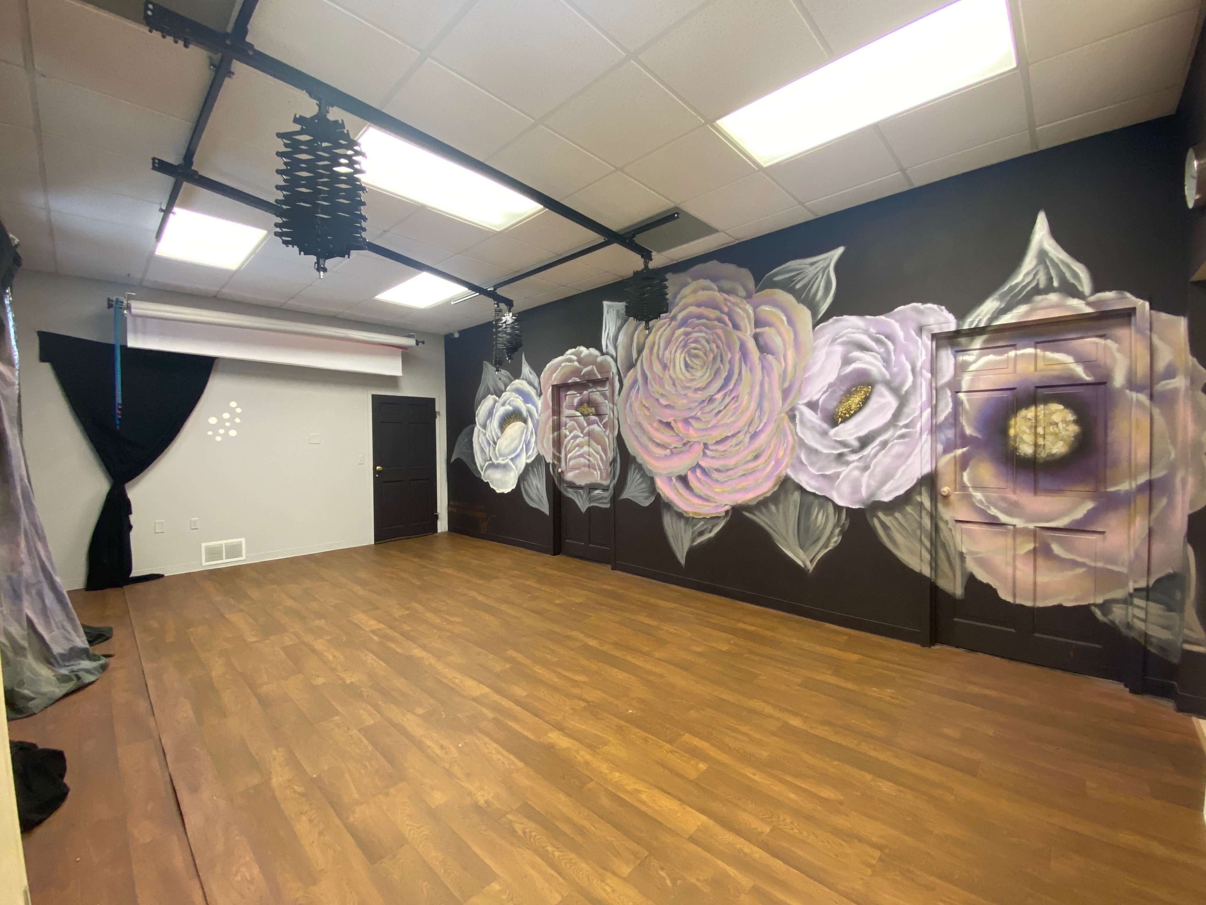 A spacious room featuring a mural of large flowers on a dark wall and a wooden floor.