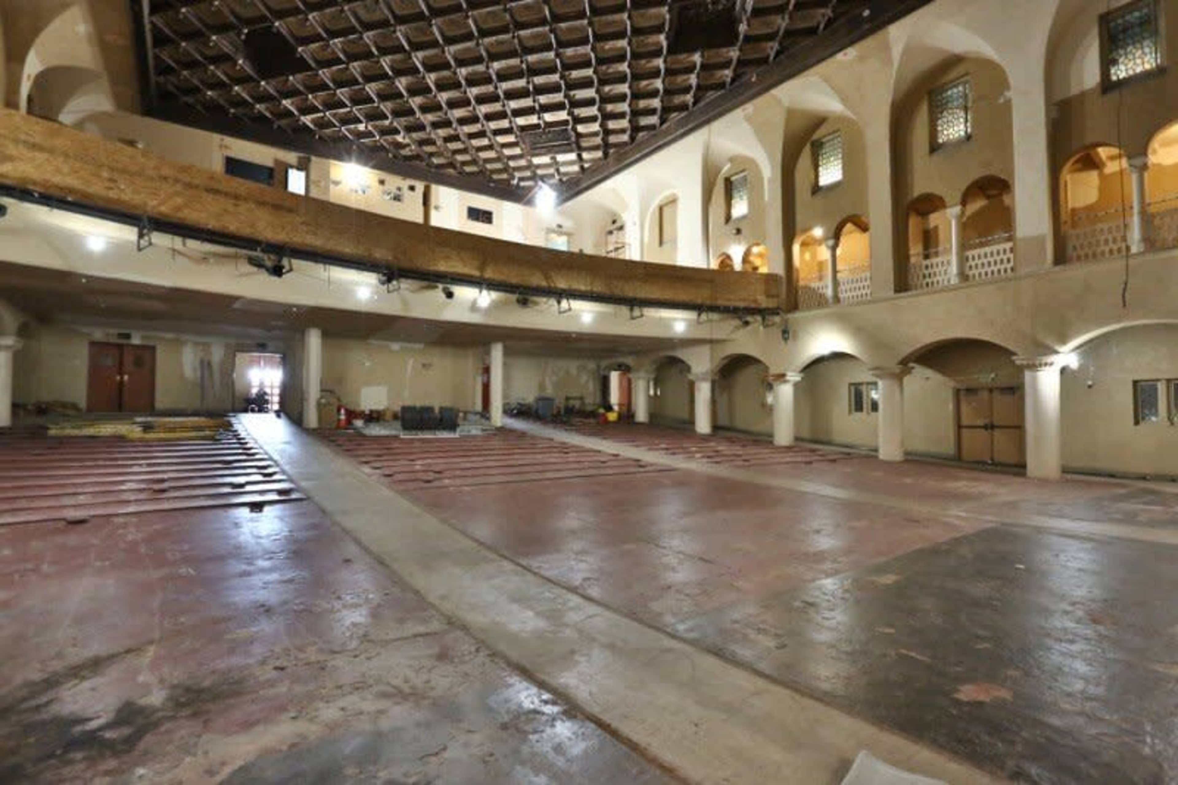 A large, empty interior space with a wooden balcony and construction materials scattered on the floor.
