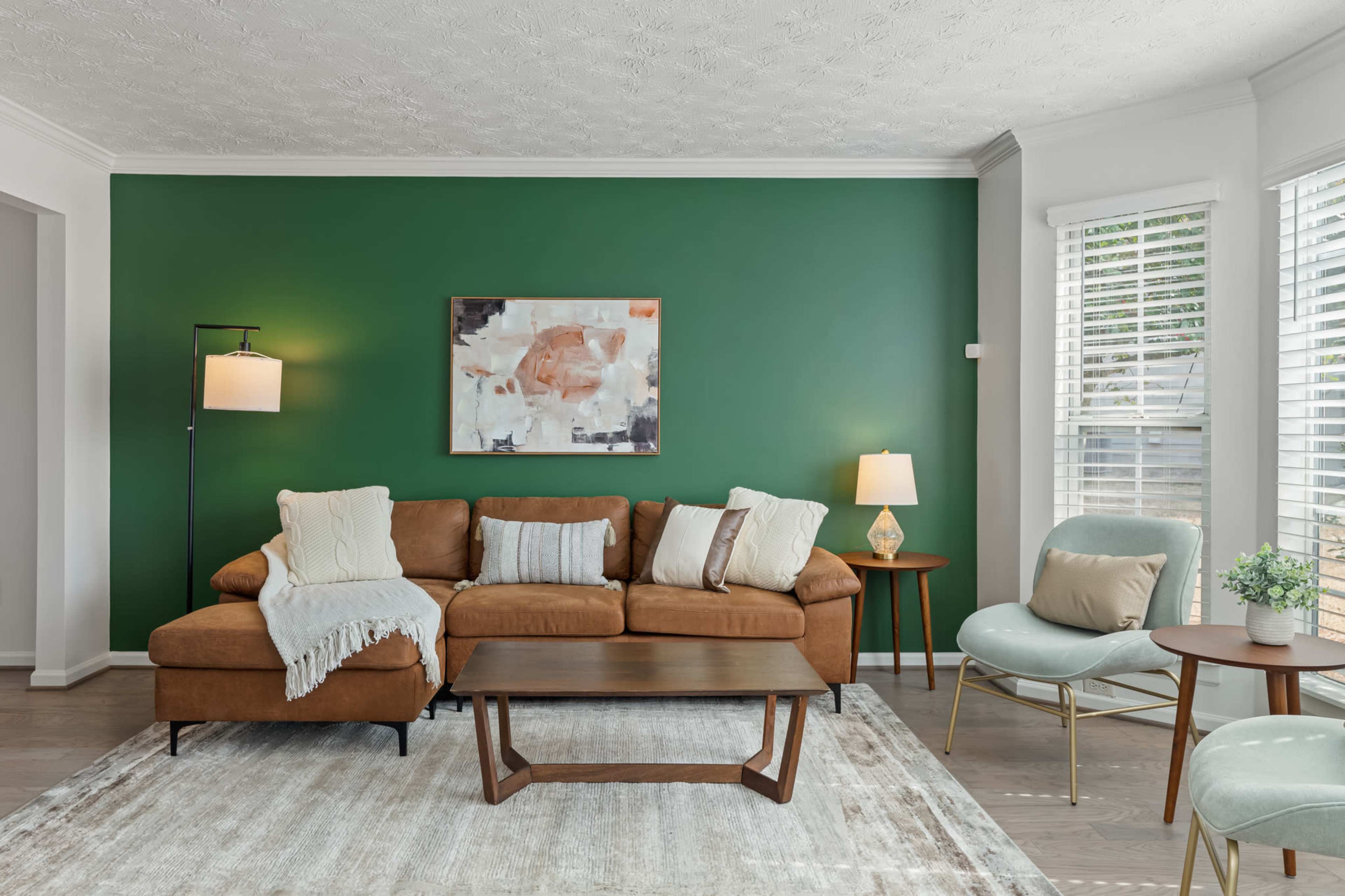 A living room featuring a brown sectional sofa, a light blue accent chair, a wooden coffee table, and a green accent wall.