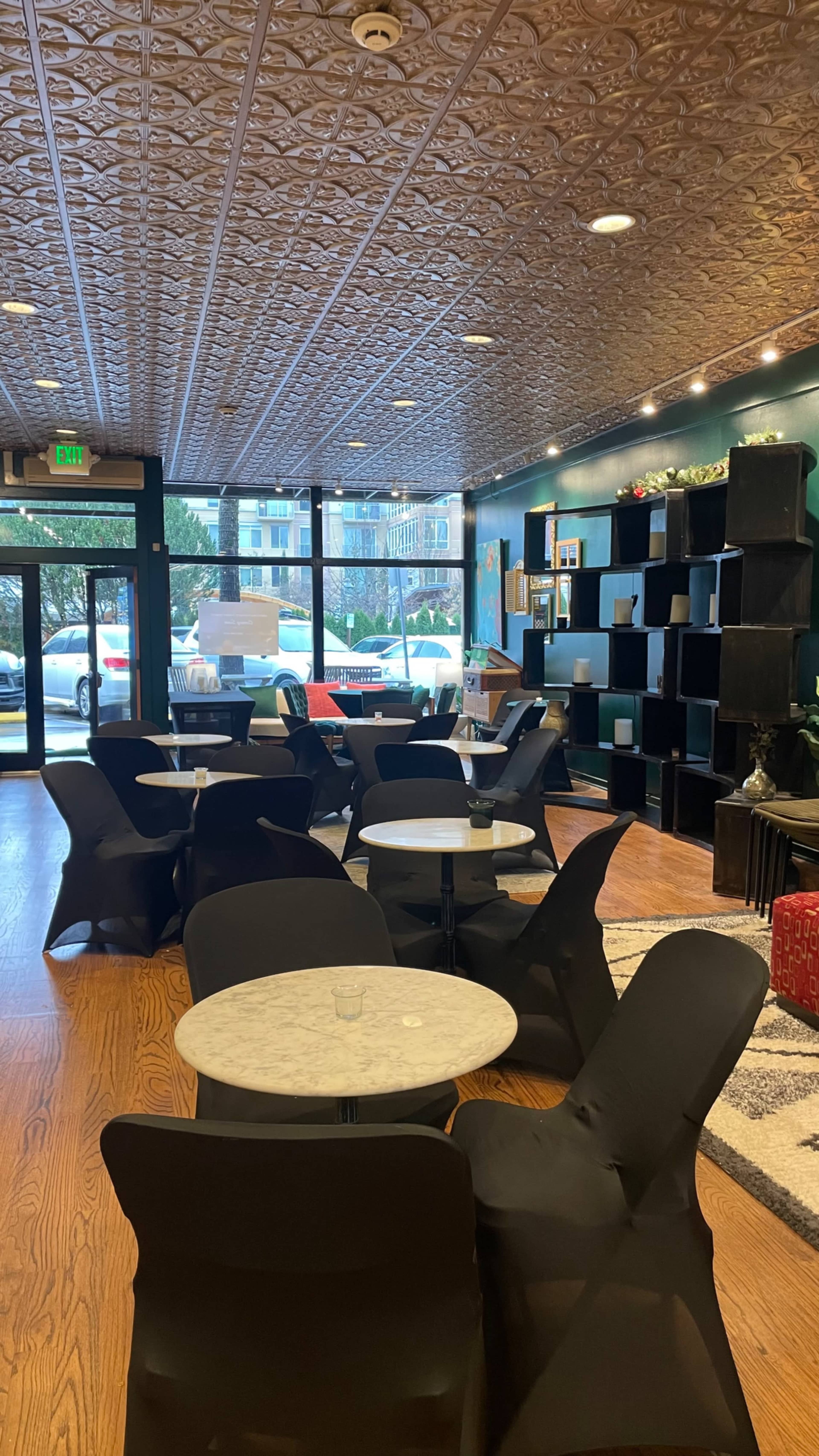The image shows a modern café interior with several round marble tables and black chairs, featuring wooden flooring and a patterned ceiling.