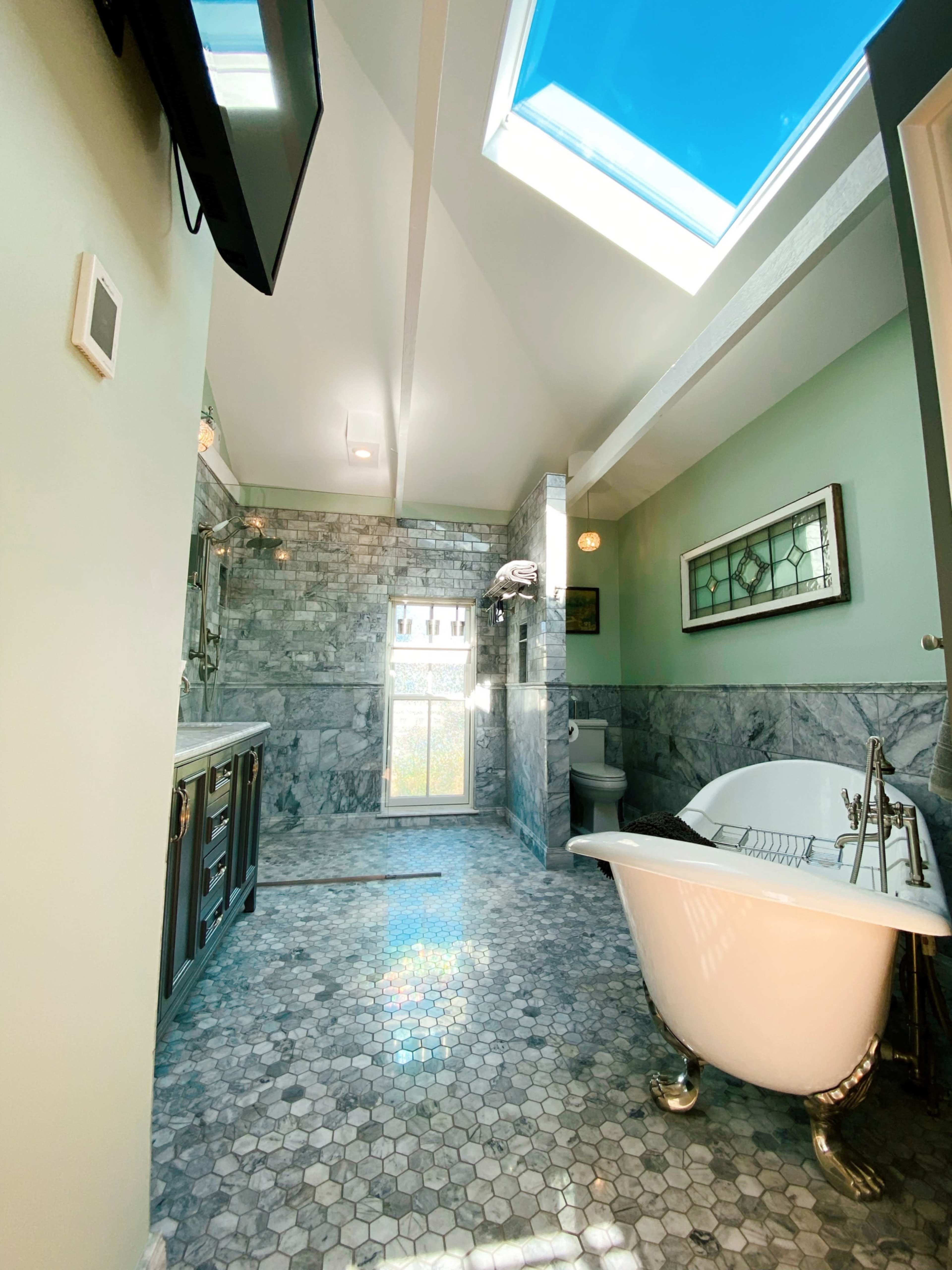 A modern bathroom with a freestanding bathtub, hexagonal tile flooring, and a skylight illuminating the space.