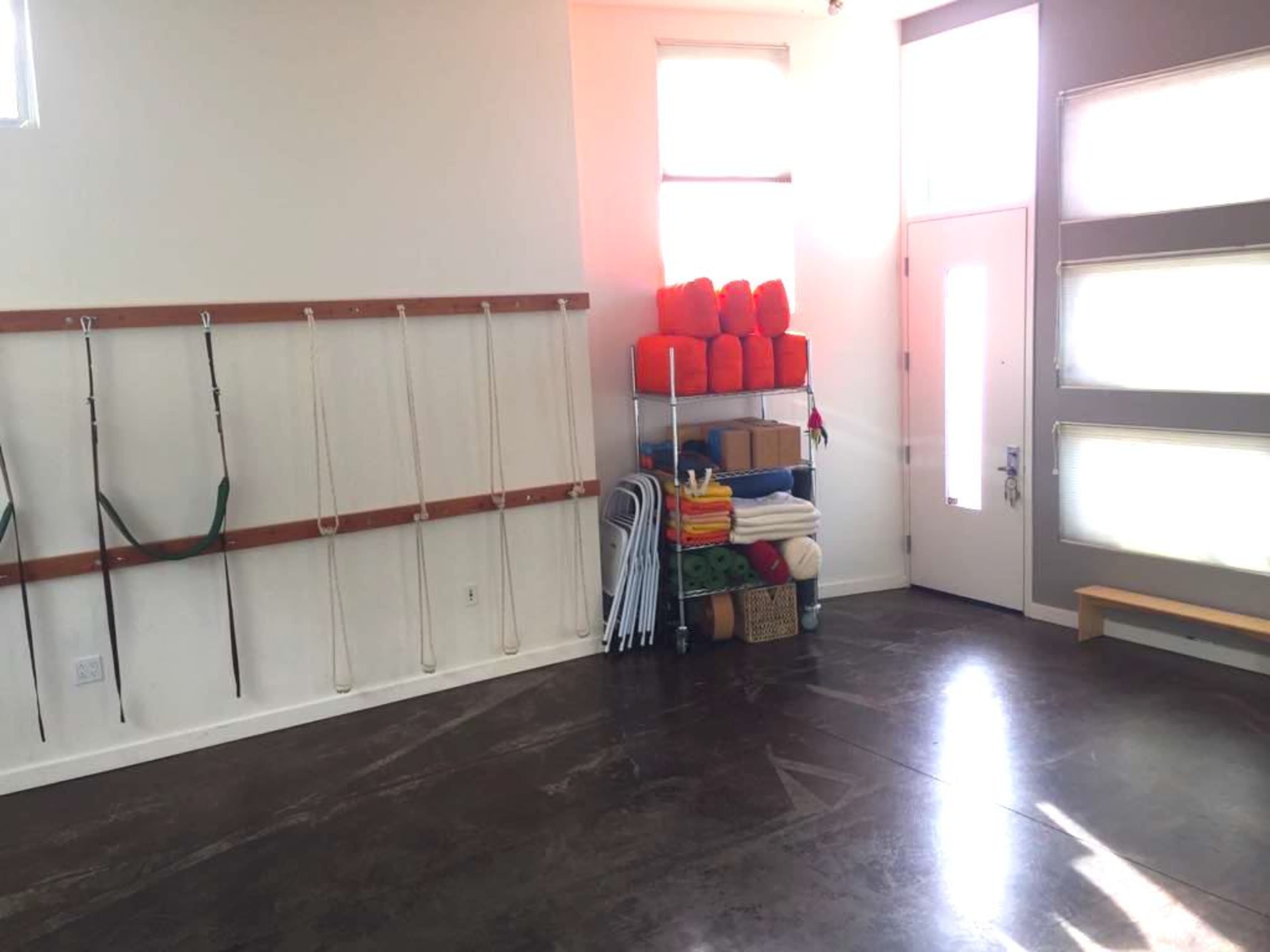 A spacious room with a wall-mounted storage system for ropes and a stack of neatly organized colorful bags and items near the entrance.