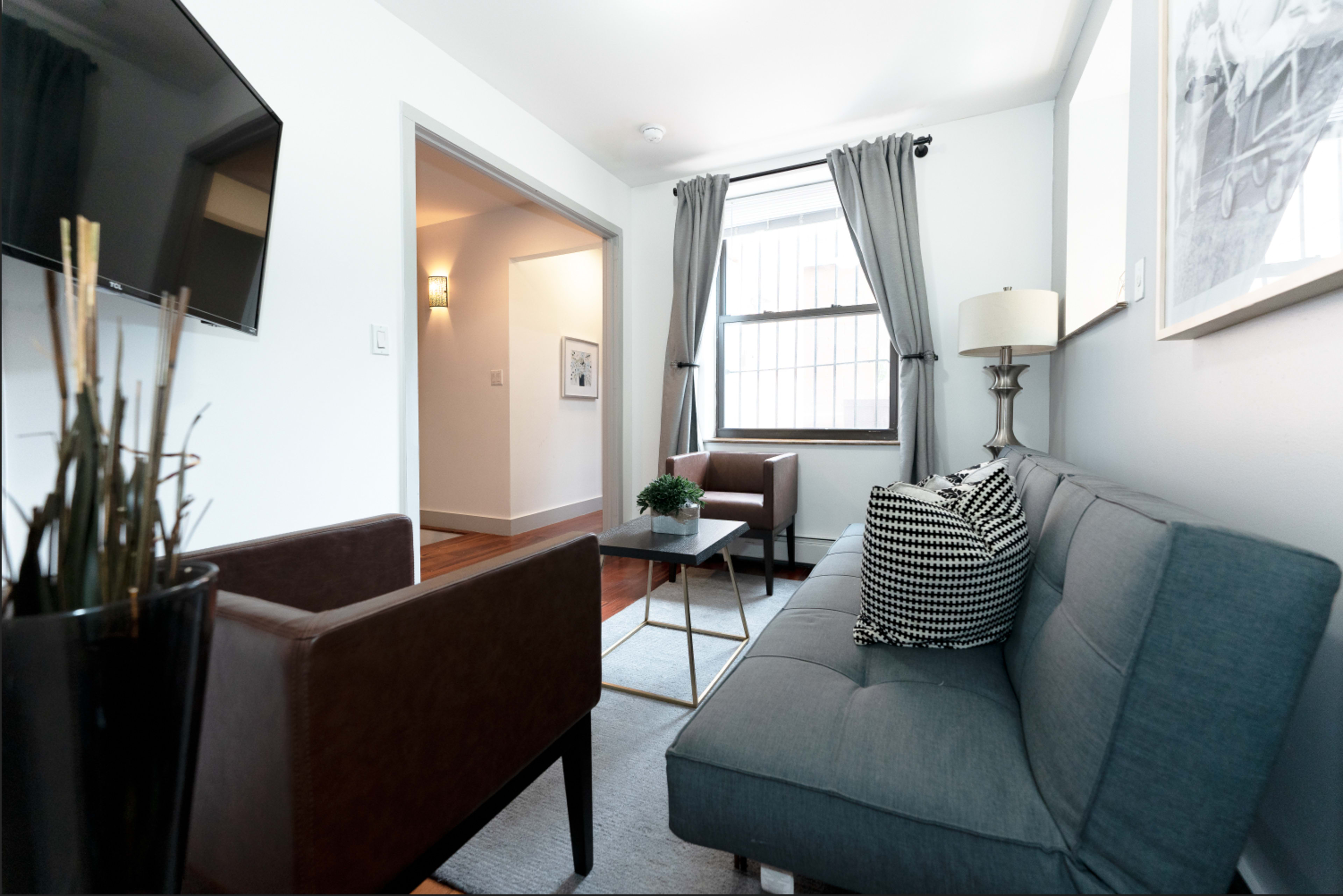 A modern living room with a gray sofa, two brown chairs, a small coffee table, and a television mounted on the wall.