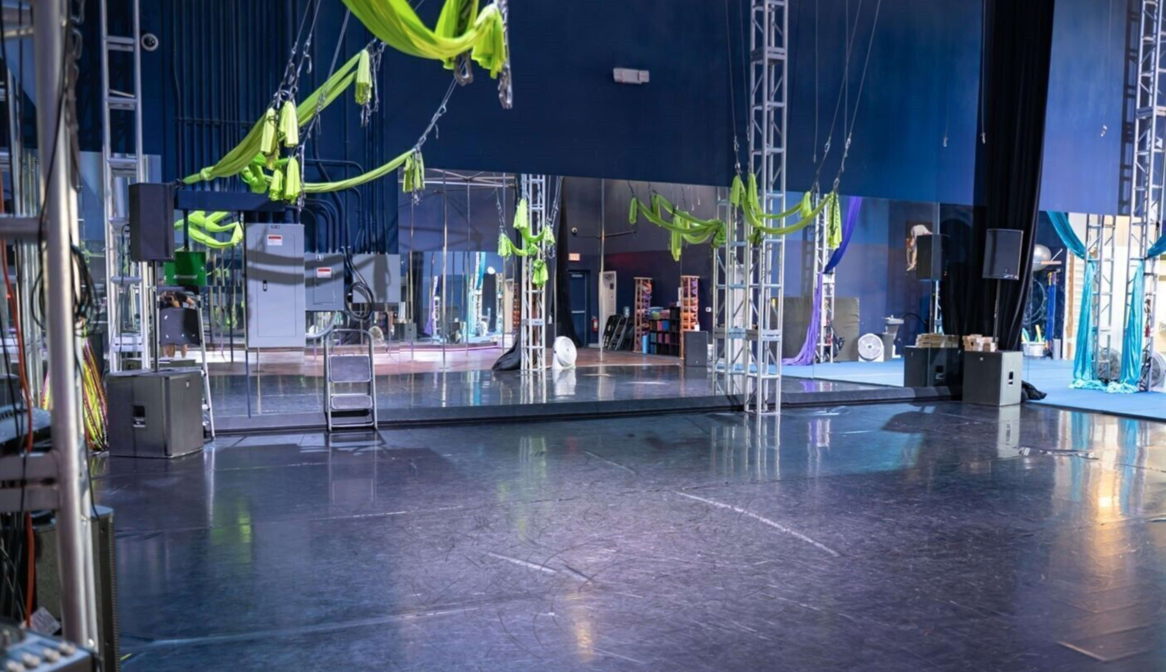 An empty dance studio with large mirrors, suspended aerial silks, and various staging equipment.