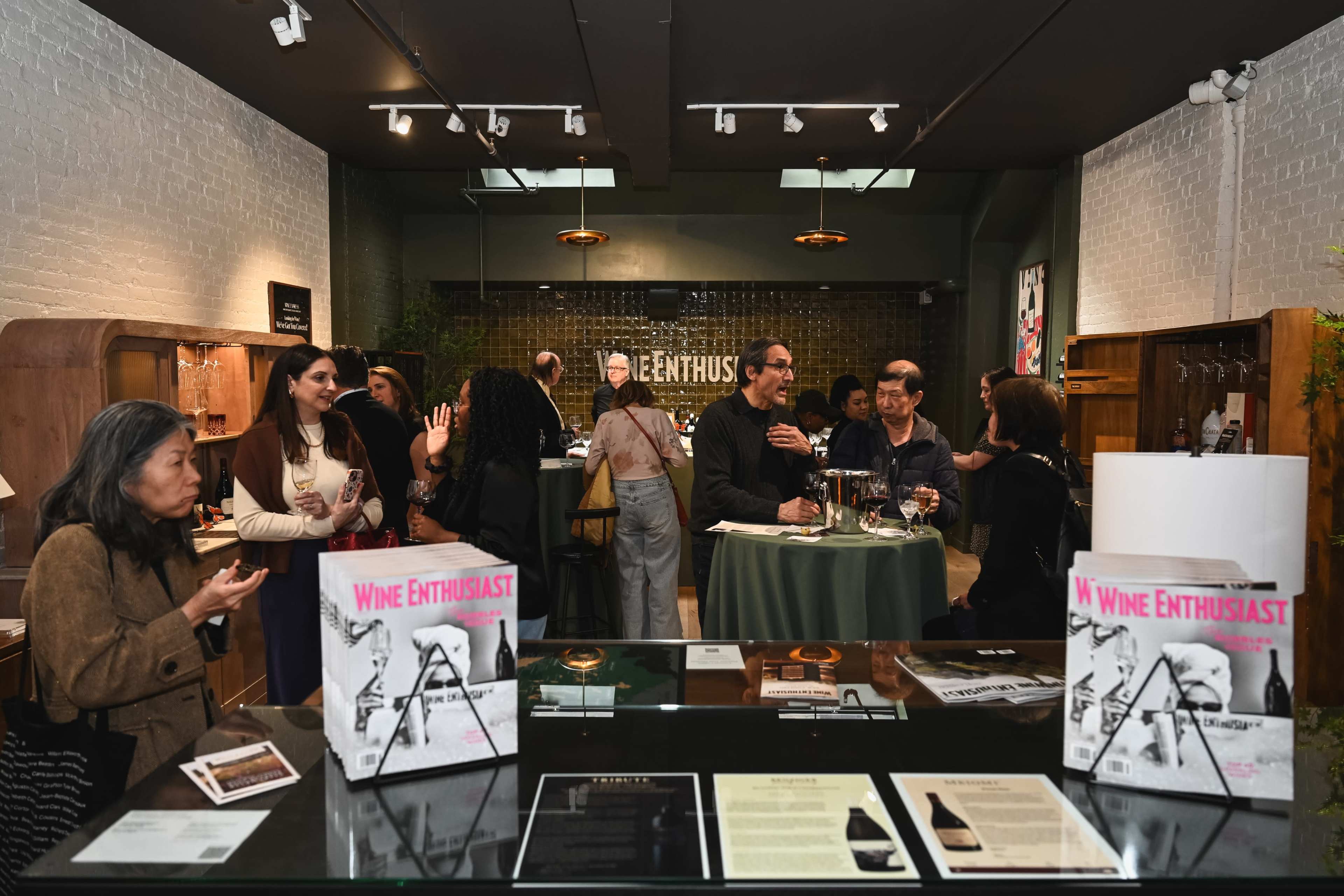 A group of people mingles and explores a wine tasting event in a stylish indoor space with tables displaying wine-related materials.