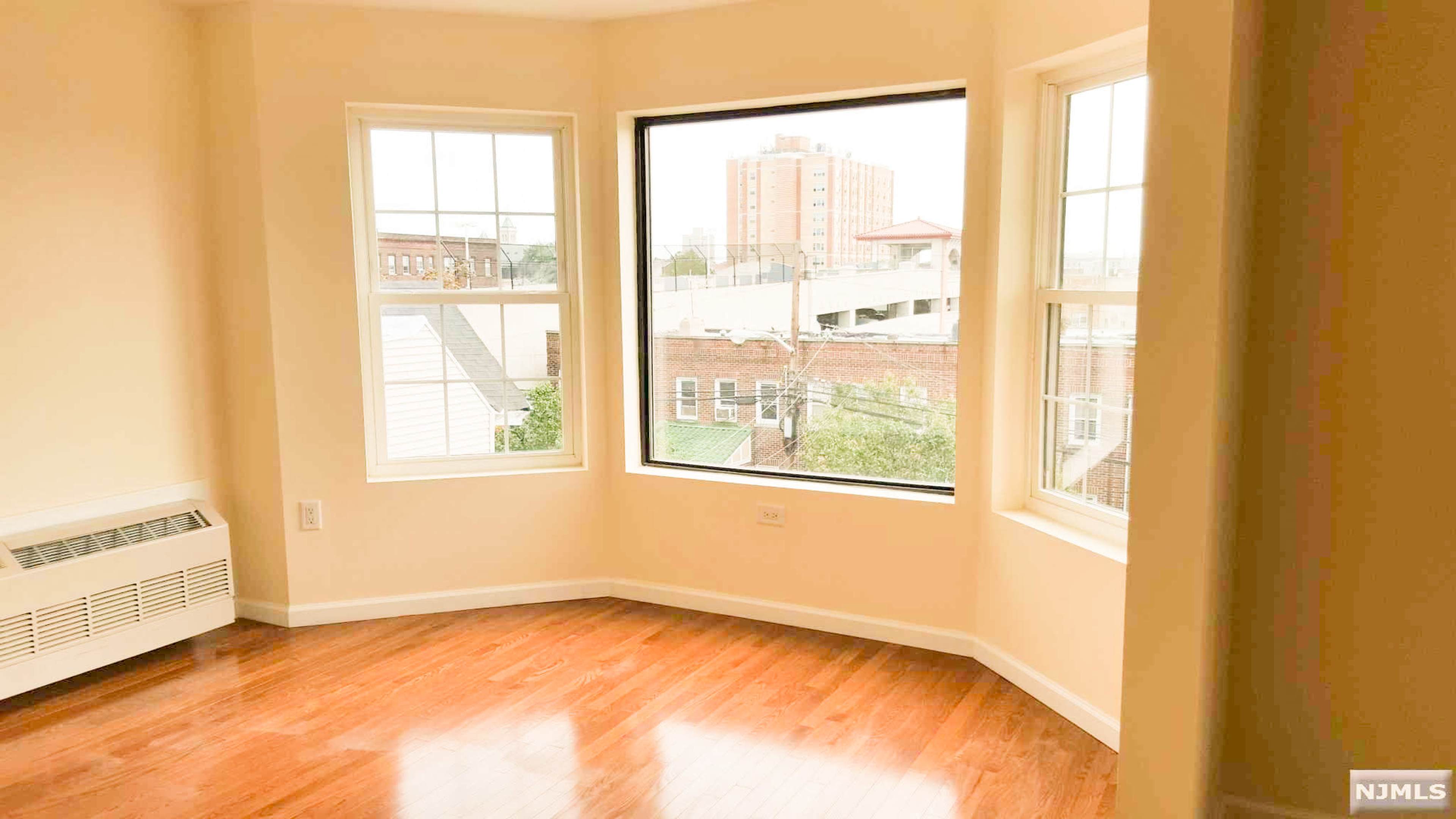 The image shows a bright room with large windows and hardwood flooring.