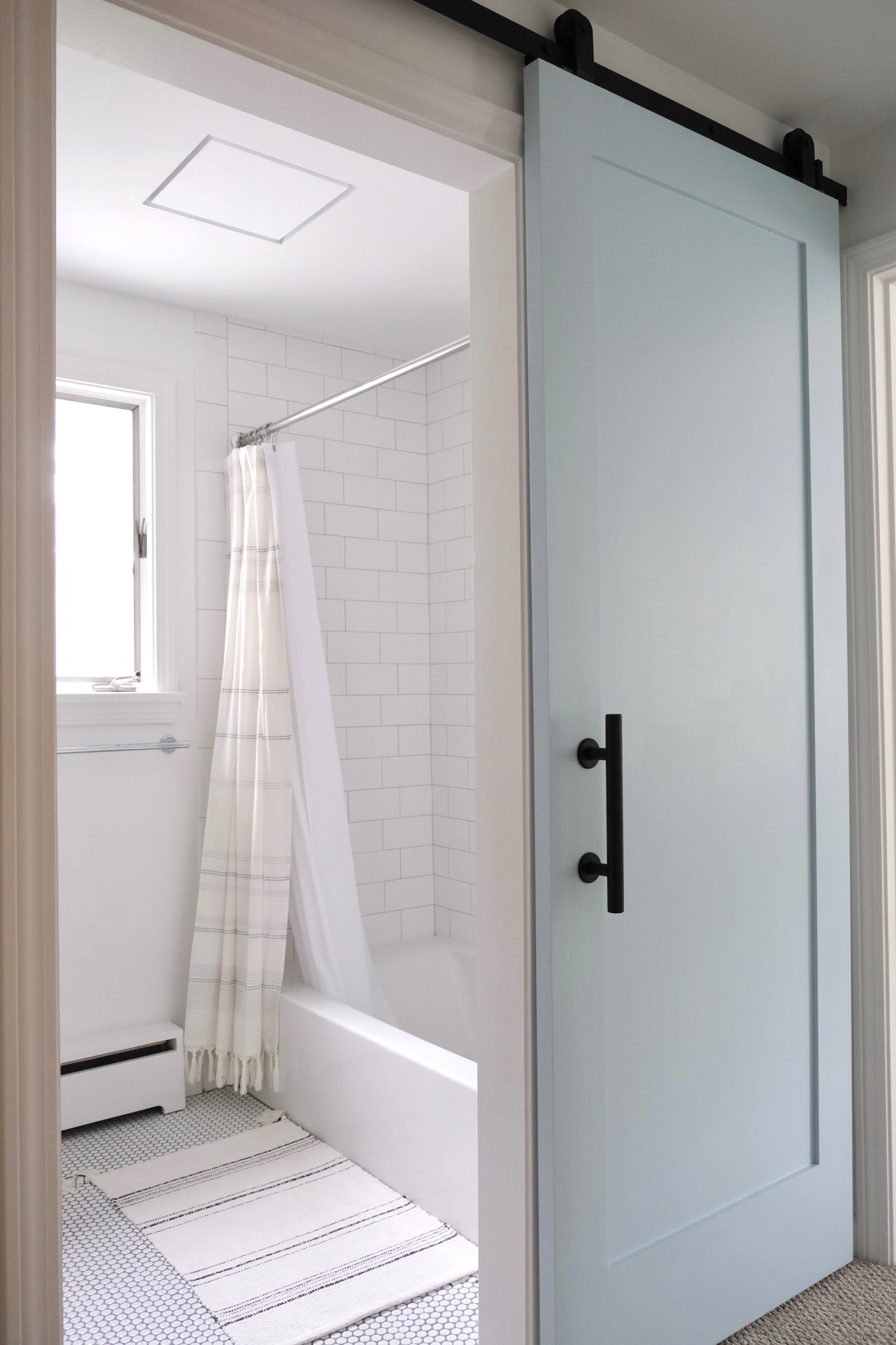 A light blue sliding door opens to a bathroom featuring white tile walls, a shower curtain, and a patterned rug.