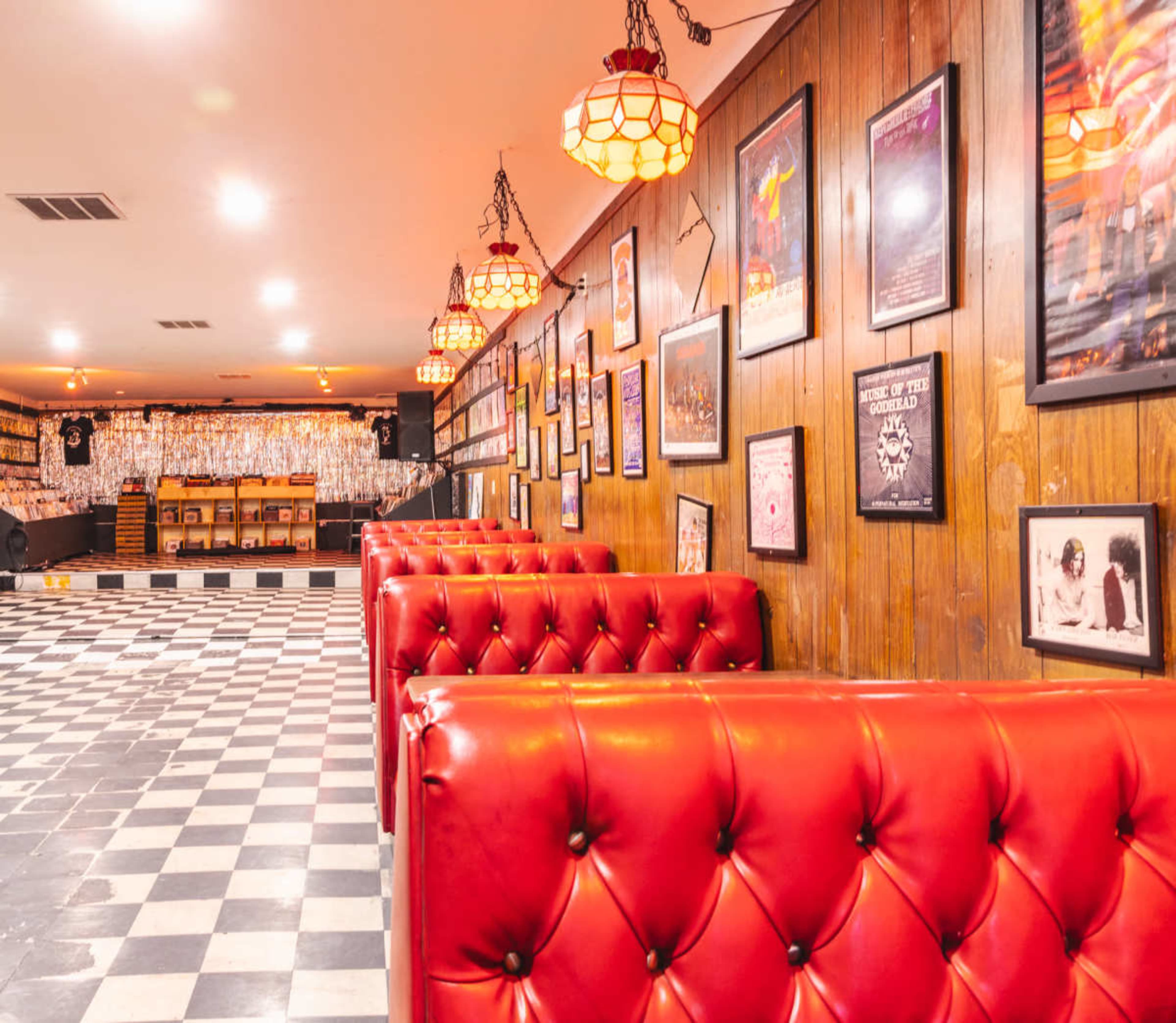 The image shows a retro-style cafe or bar interior with red tufted booths, checkered flooring, and walls adorned with framed artwork and posters.