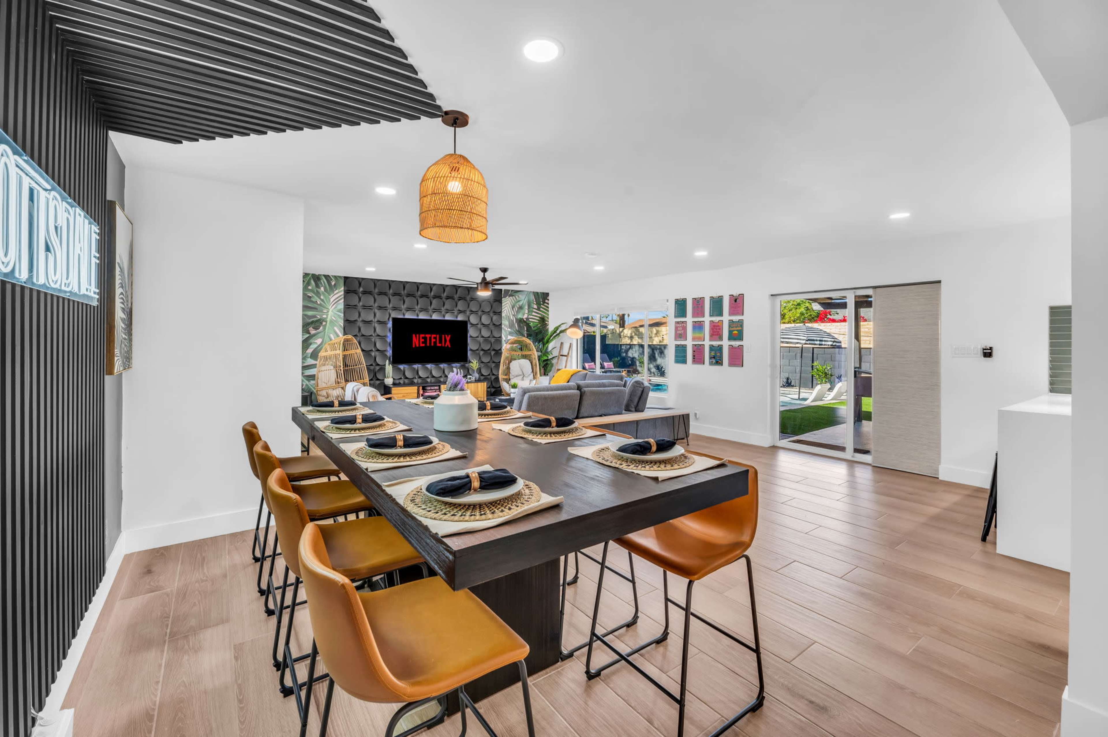 A modern dining area features a large wooden table with black plates and stylish chairs, adjacent to a living space with a Netflix screen.