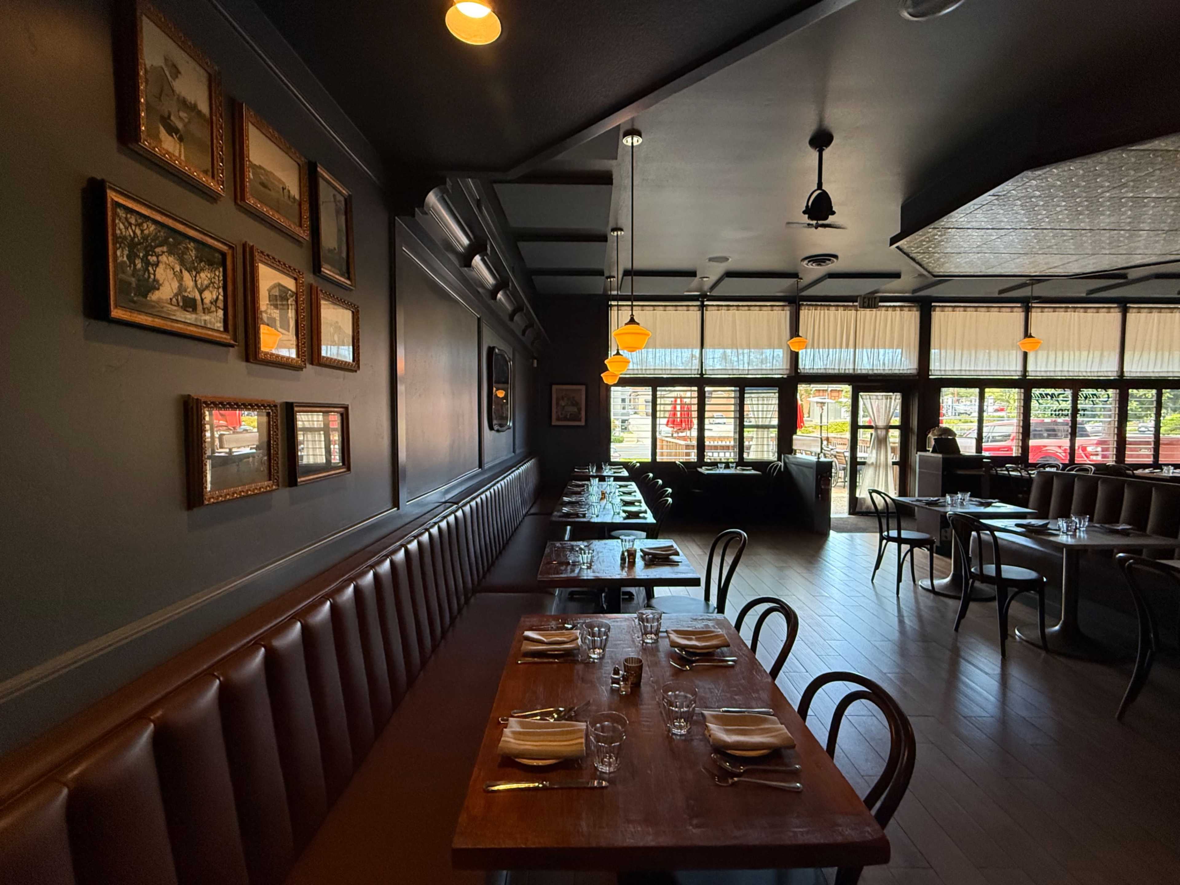 The image shows the interior of a restaurant featuring wooden tables, brown upholstered seating, and framed artwork on the walls.