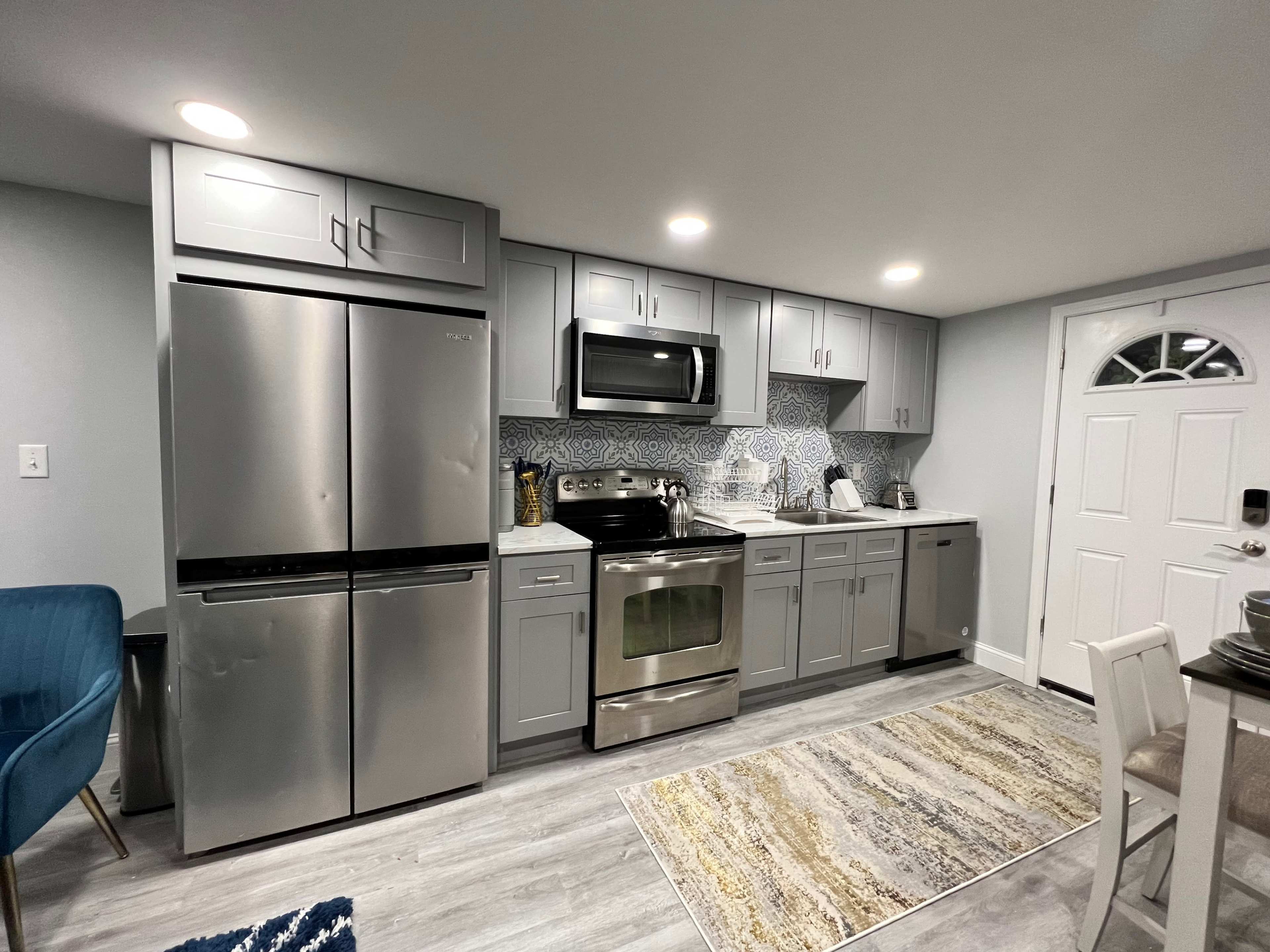 A modern kitchen with stainless steel appliances, gray cabinets, and a patterned backsplash, alongside a door leading outside.